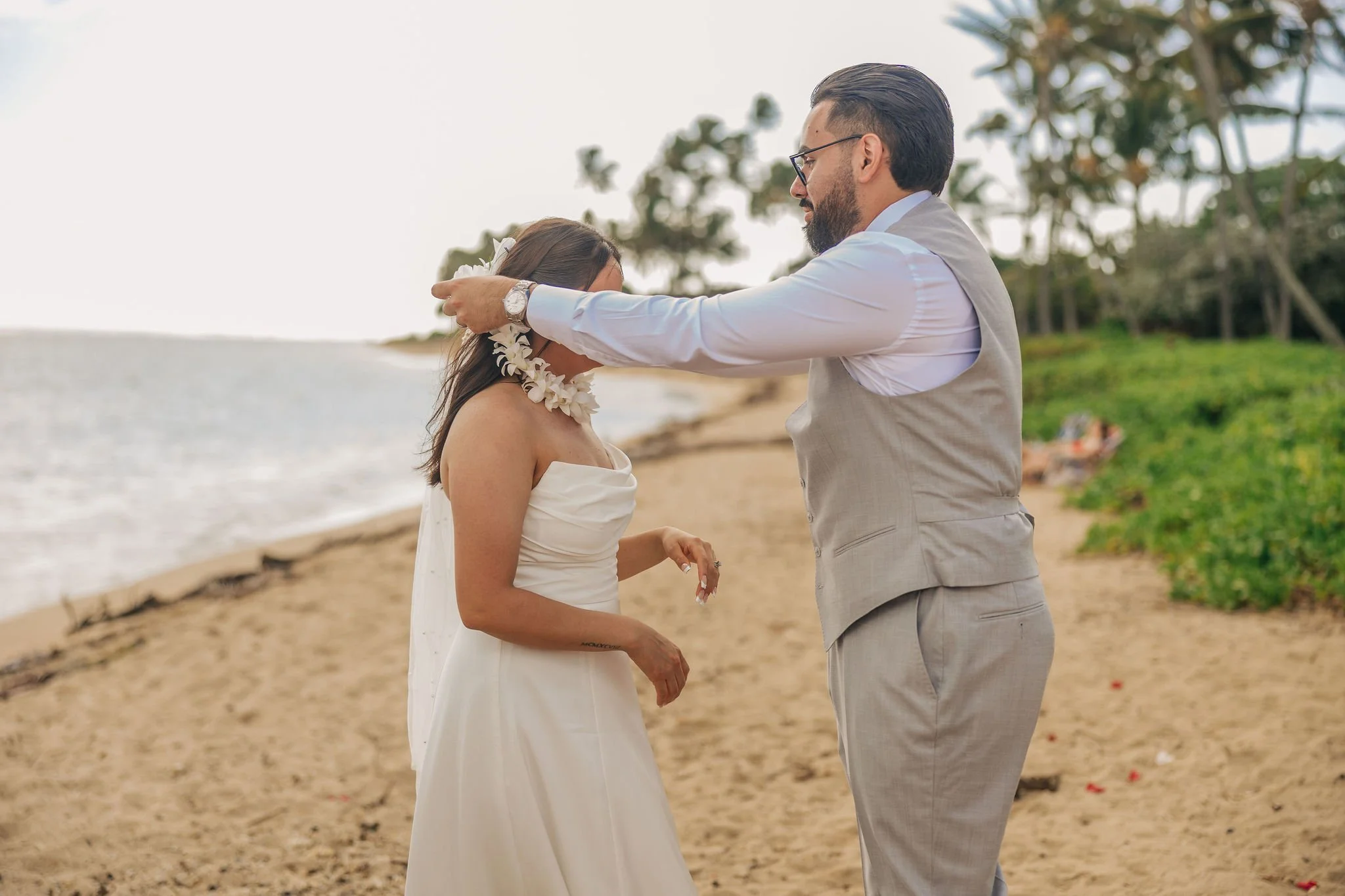 A man placing a necklace on a woman on the beach during sunset.