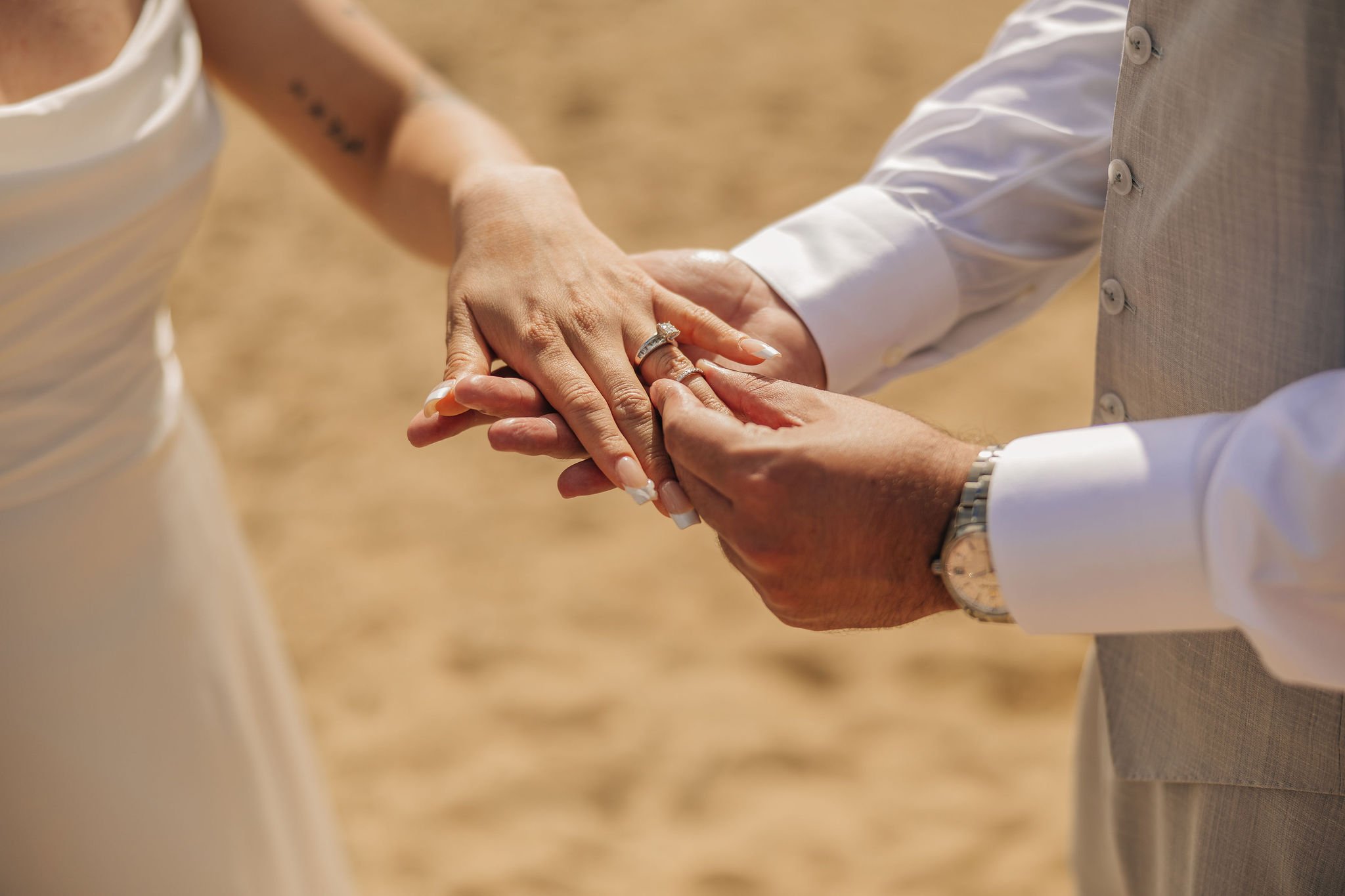 Close-up of a couple holding hands during wedding ceremony, with focus on wedding rings on their fingers.