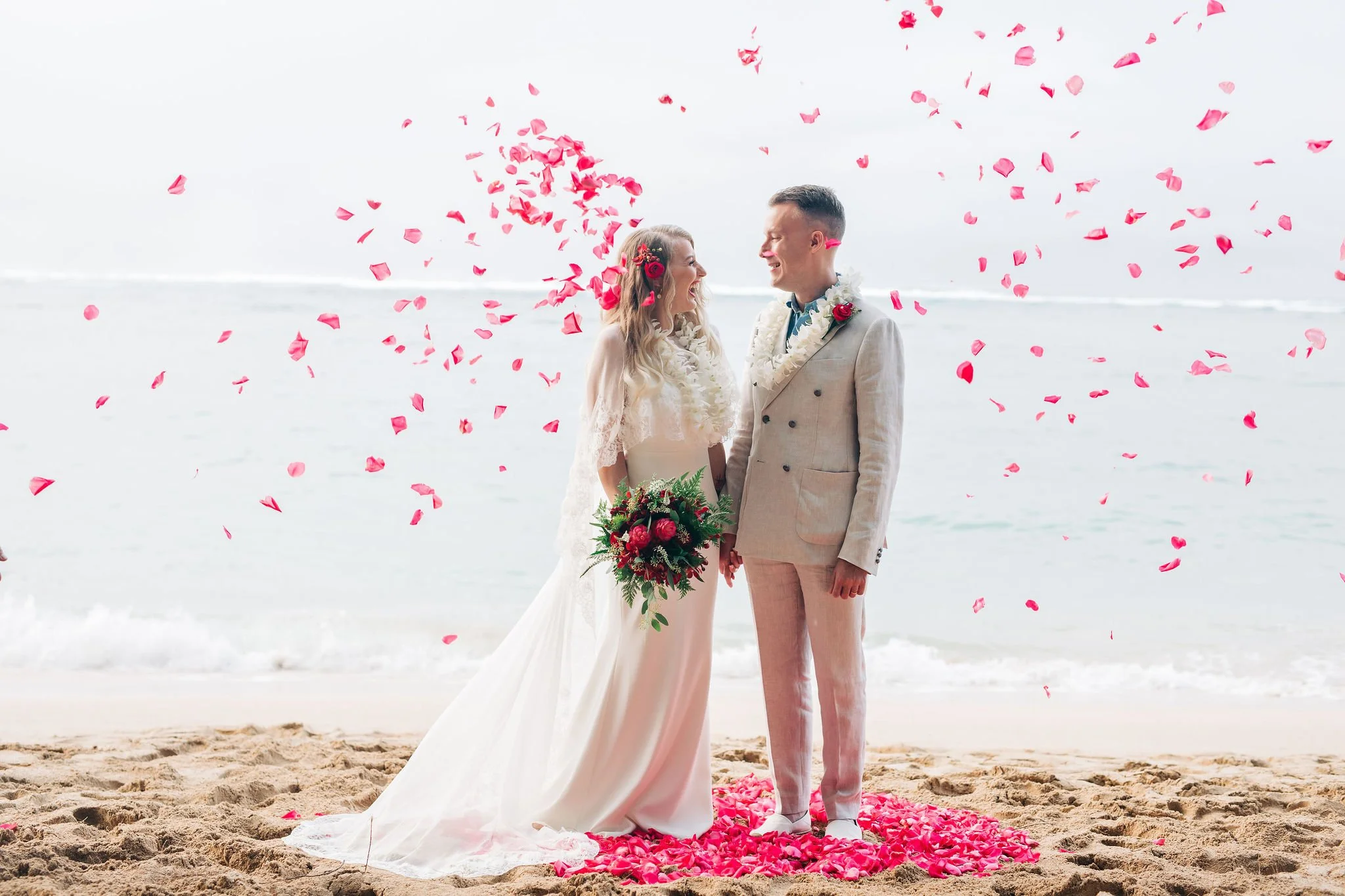Bride and groom standing on the beach with pink rose petals falling around them, wedding ceremony scene.