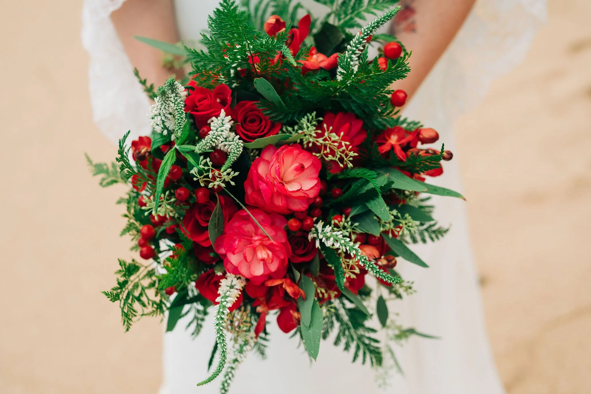 A person holding a bouquet of red and pink roses, greenery, and small white accents.