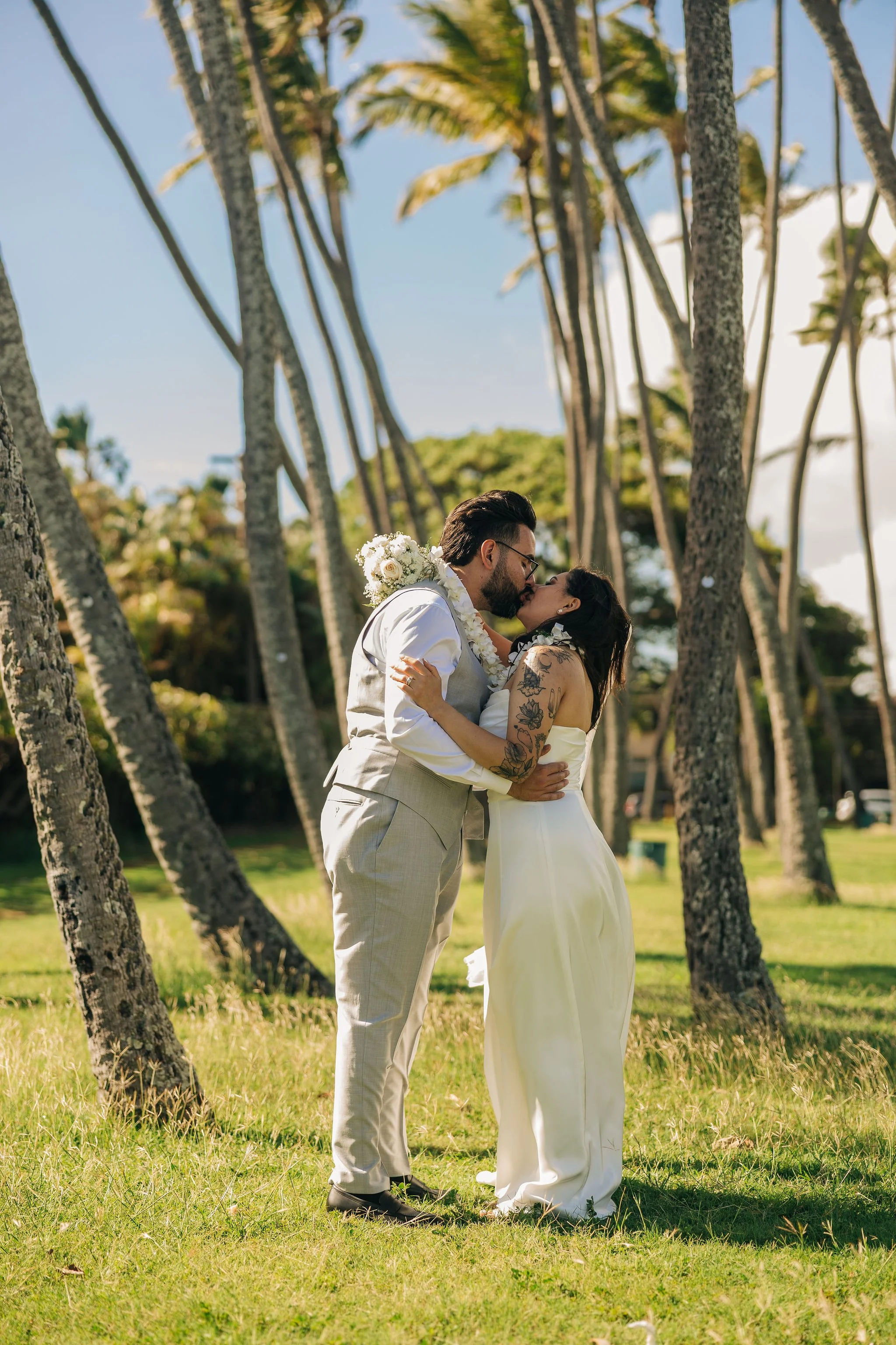 A bride and groom sharing a kiss outdoors among tall palm trees on a sunny day