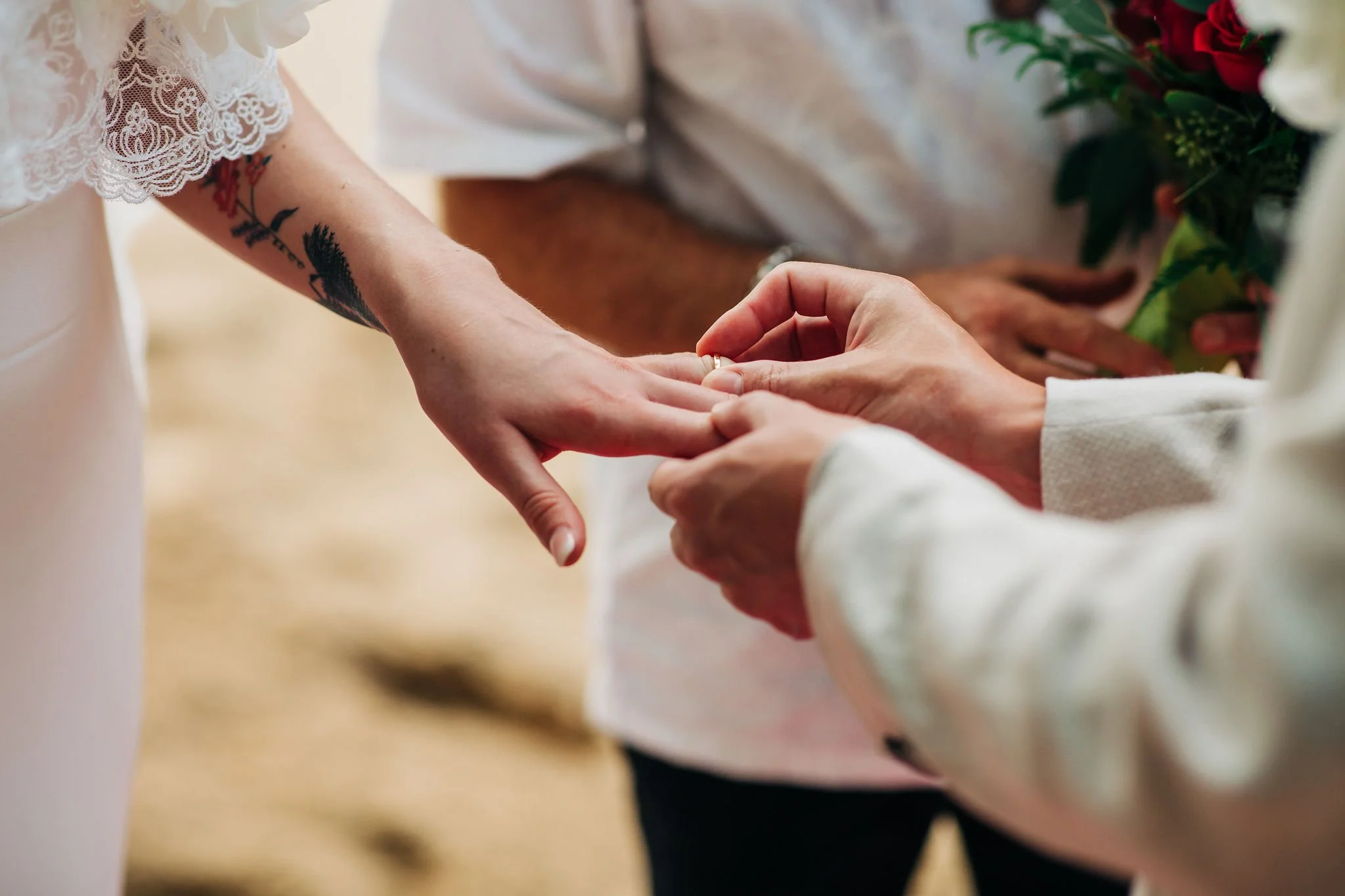 A person wearing a white lace dress is placing a ring on another person's finger during a wedding ceremony.