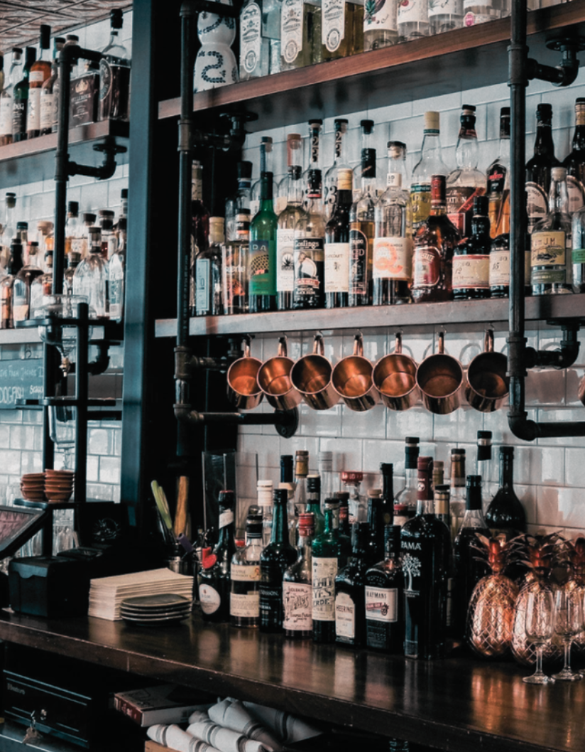 Shelves of liquor bottles and copper mugs in a bar setting.
