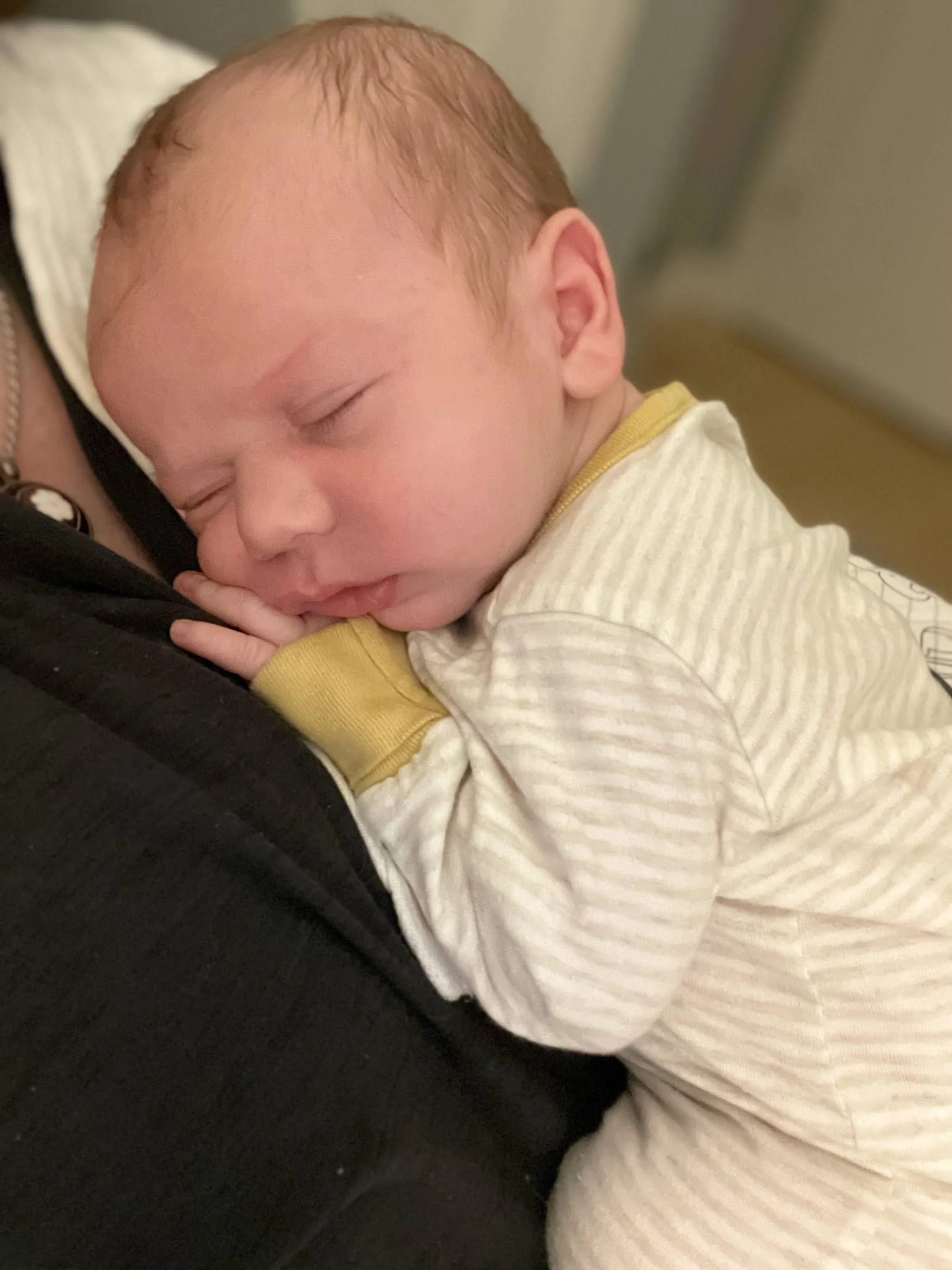 A sleeping baby with red hair resting on a person's chest, wearing a yellow and white striped shirt.