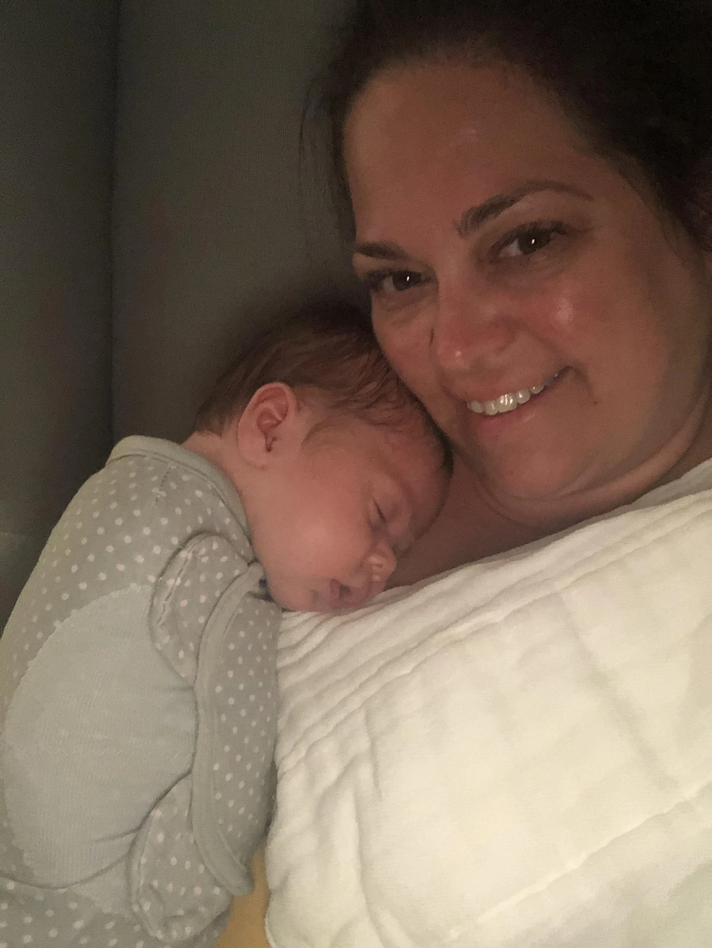 A doula and a newborn, with the child resting their head on the woman's chest, both smiling and appearing happy.