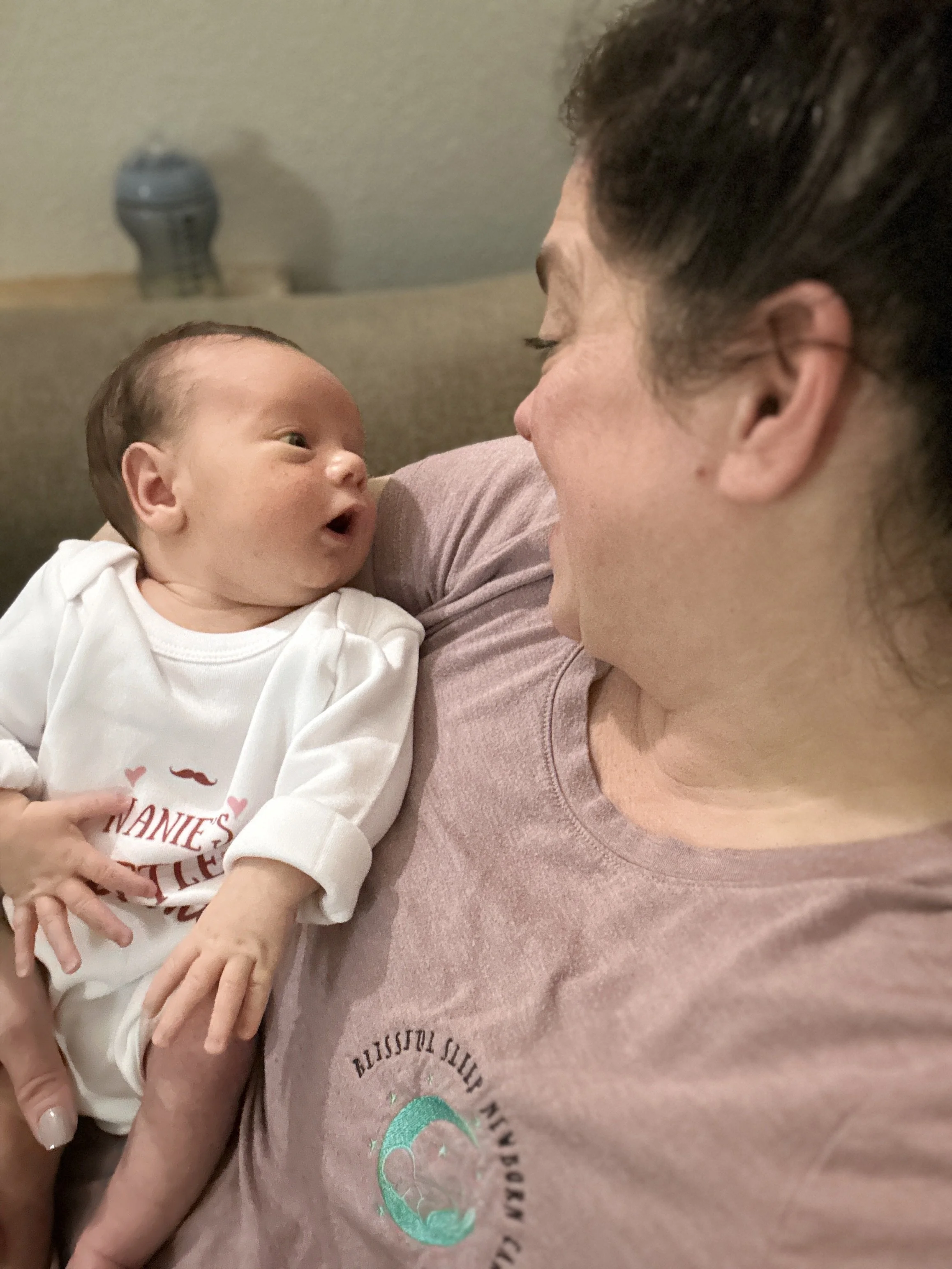 A woman holding a newborn baby and looking into the baby's eyes at close range indoors.