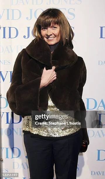 Woman smiling, wearing a dark brown fur coat and a sparkly top, standing in front of a promotional backdrop for David Jones.