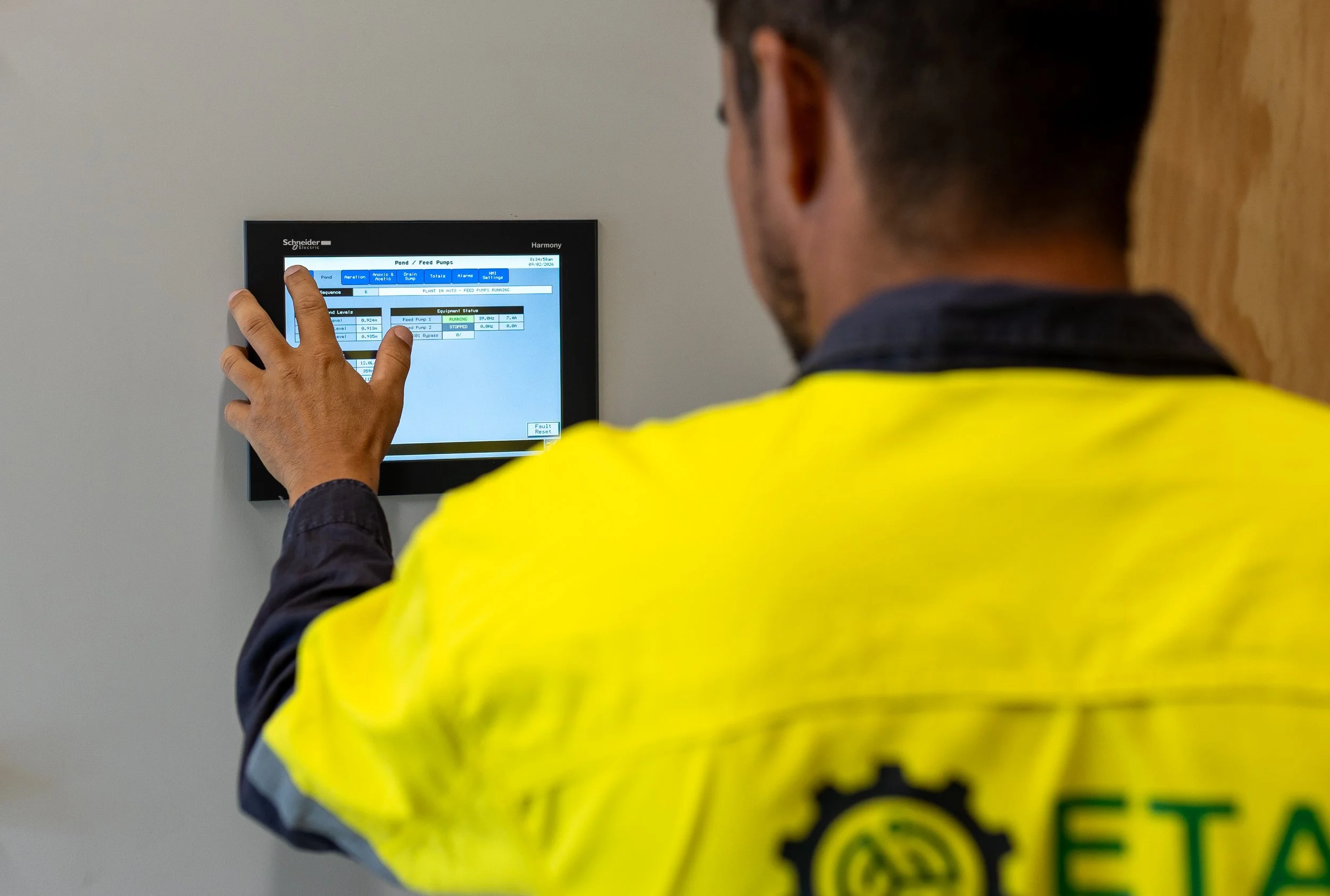 Worker in safety vest operating a digital control panel on a wall.