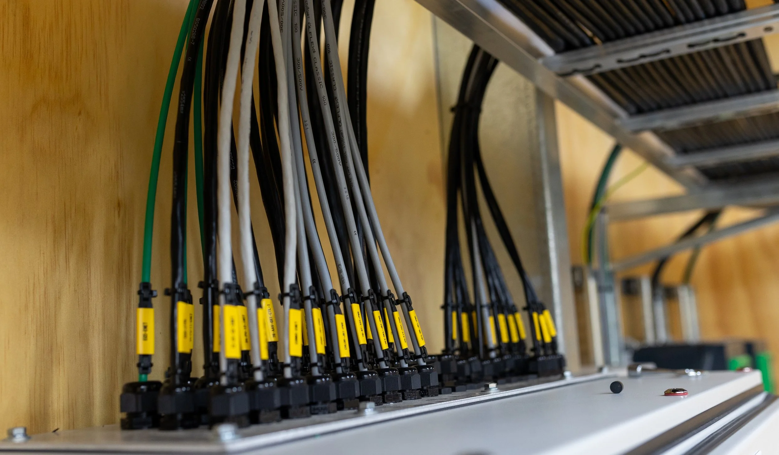 Multiple cables connected to a metal panel with yellow labels, mounted on a wooden background, in an electrical or networking setup.