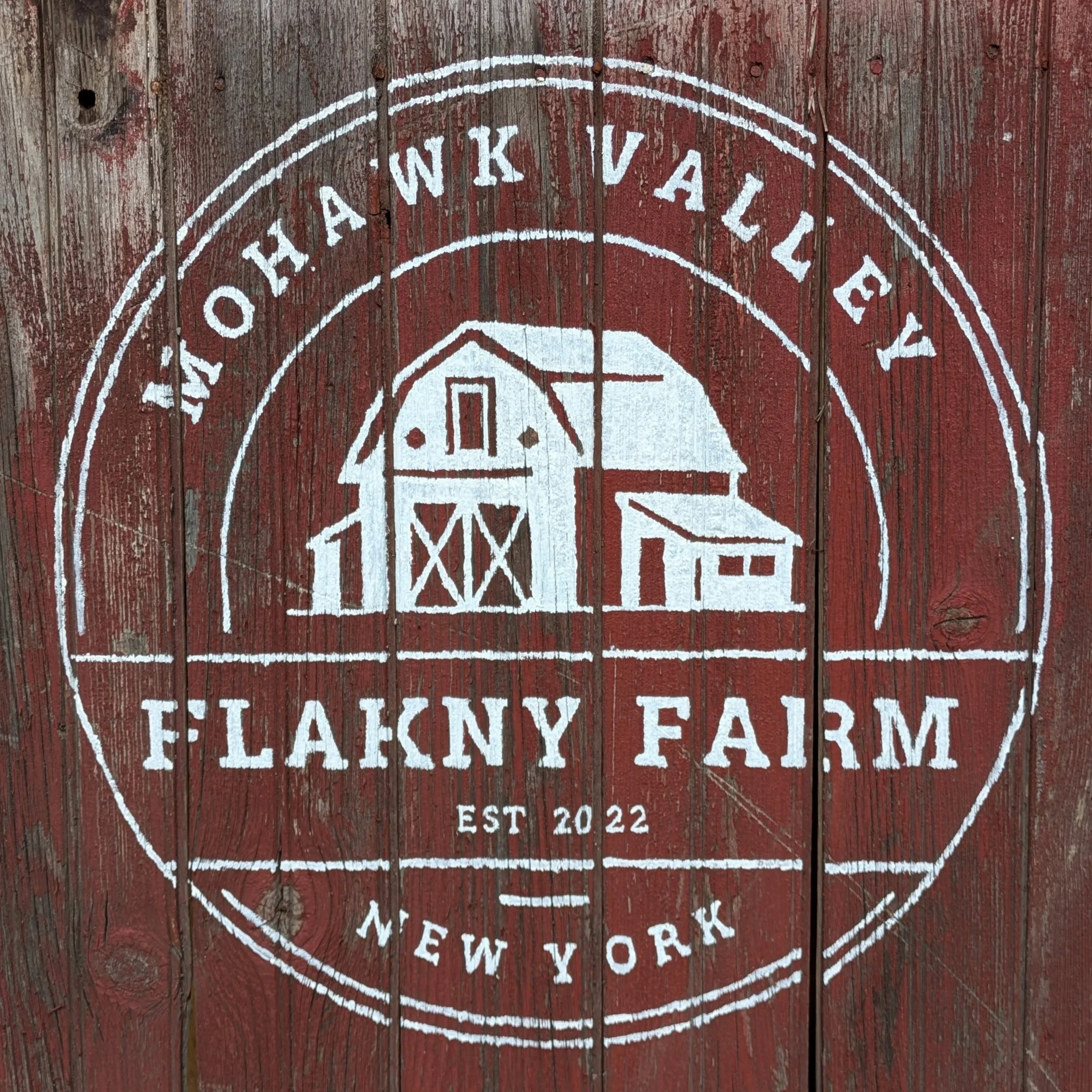 Hand-painted sign on weathered wooden planks reading 'FLAKNY Farm' with a circular border around the text.