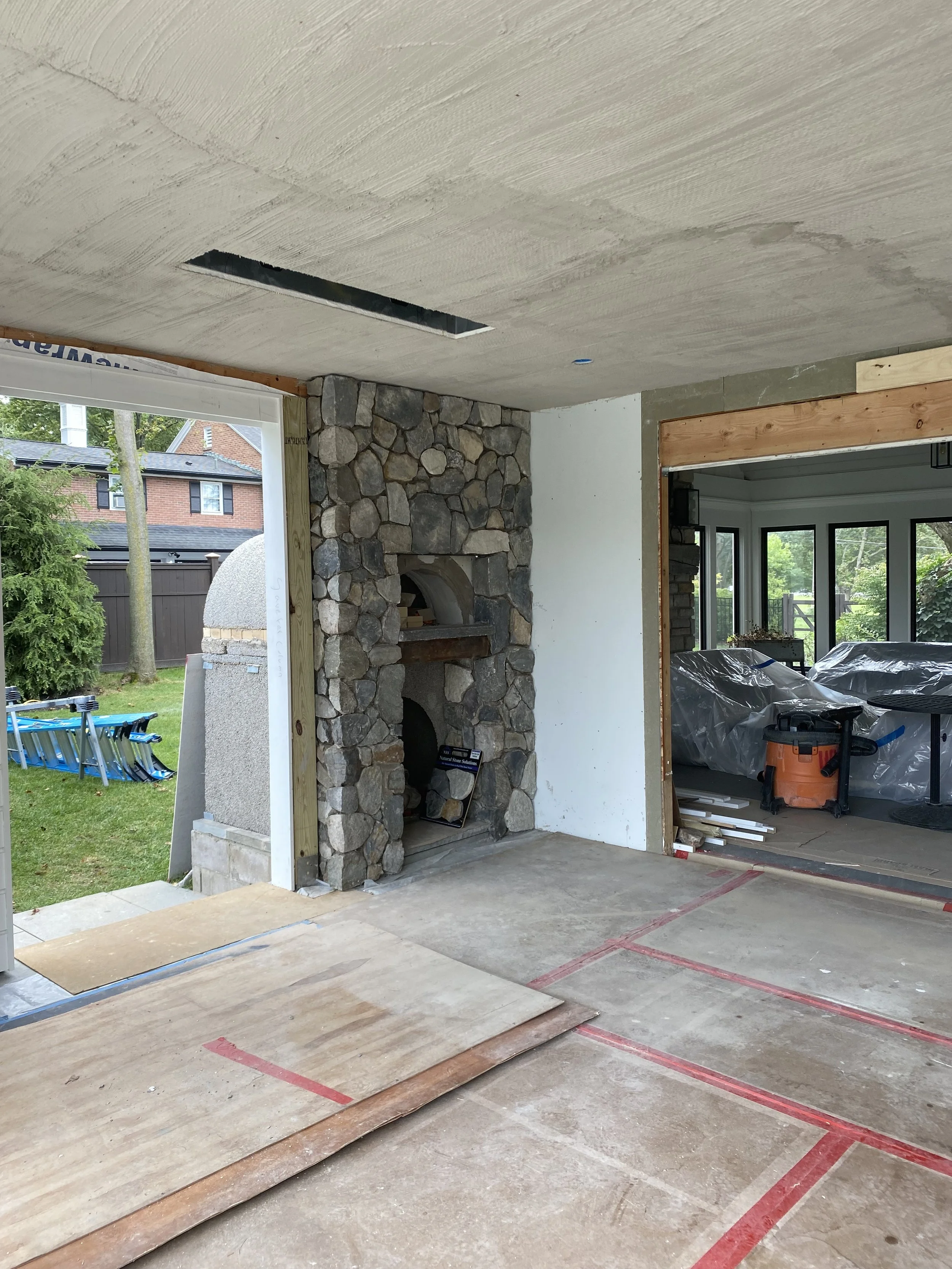 Interior of a house under construction with a stone fireplace, unfinished ceiling, and construction materials on the floor.