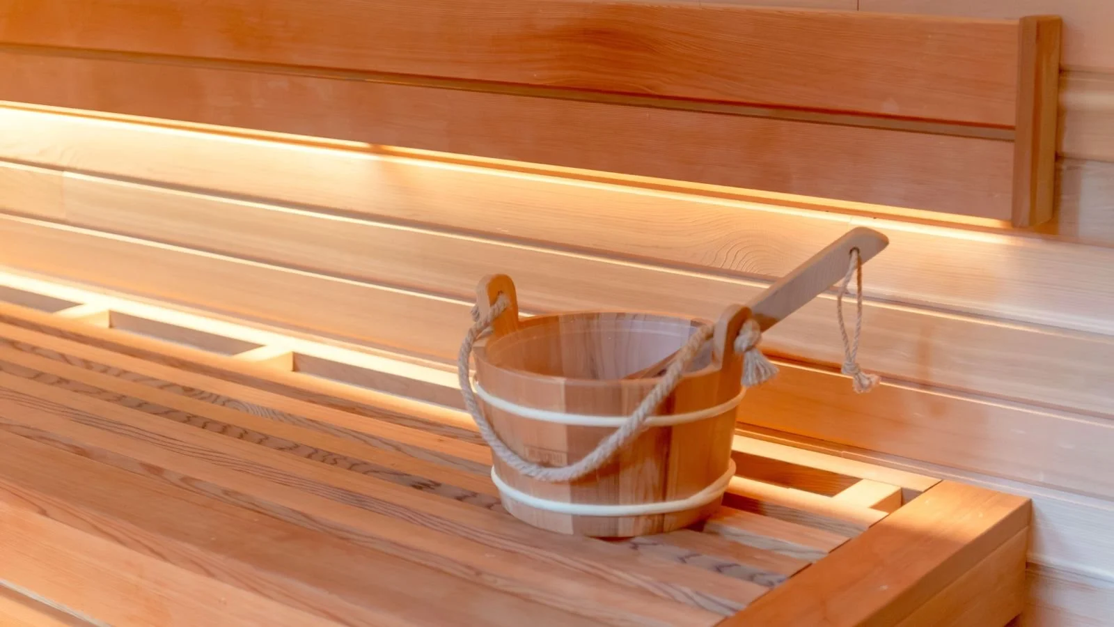 A wooden sauna bench with a wooden bucket and ladle on it.
