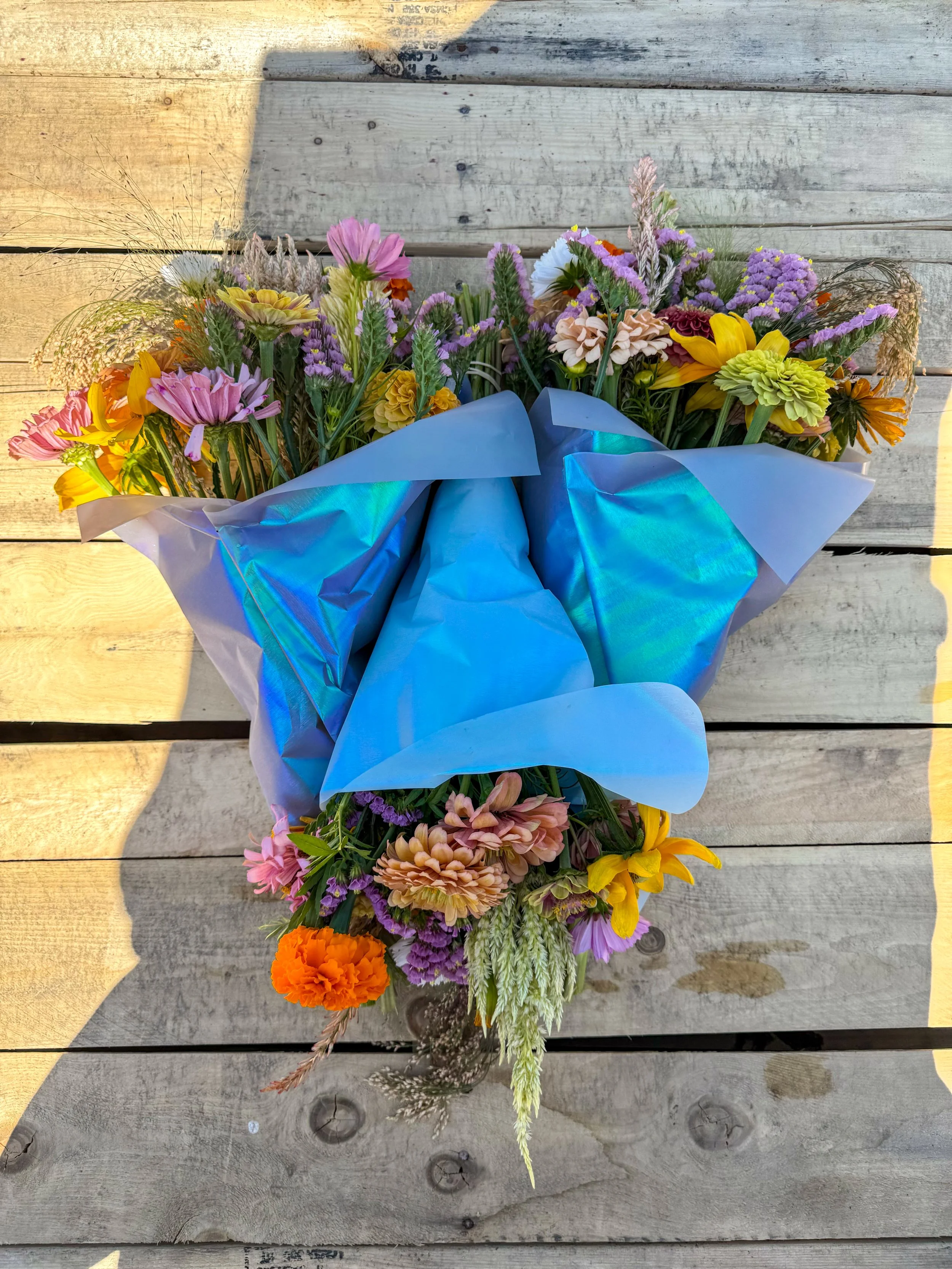 Colorful mixed flower bouquet wrapped in shiny blue paper, laid on a wooden surface.