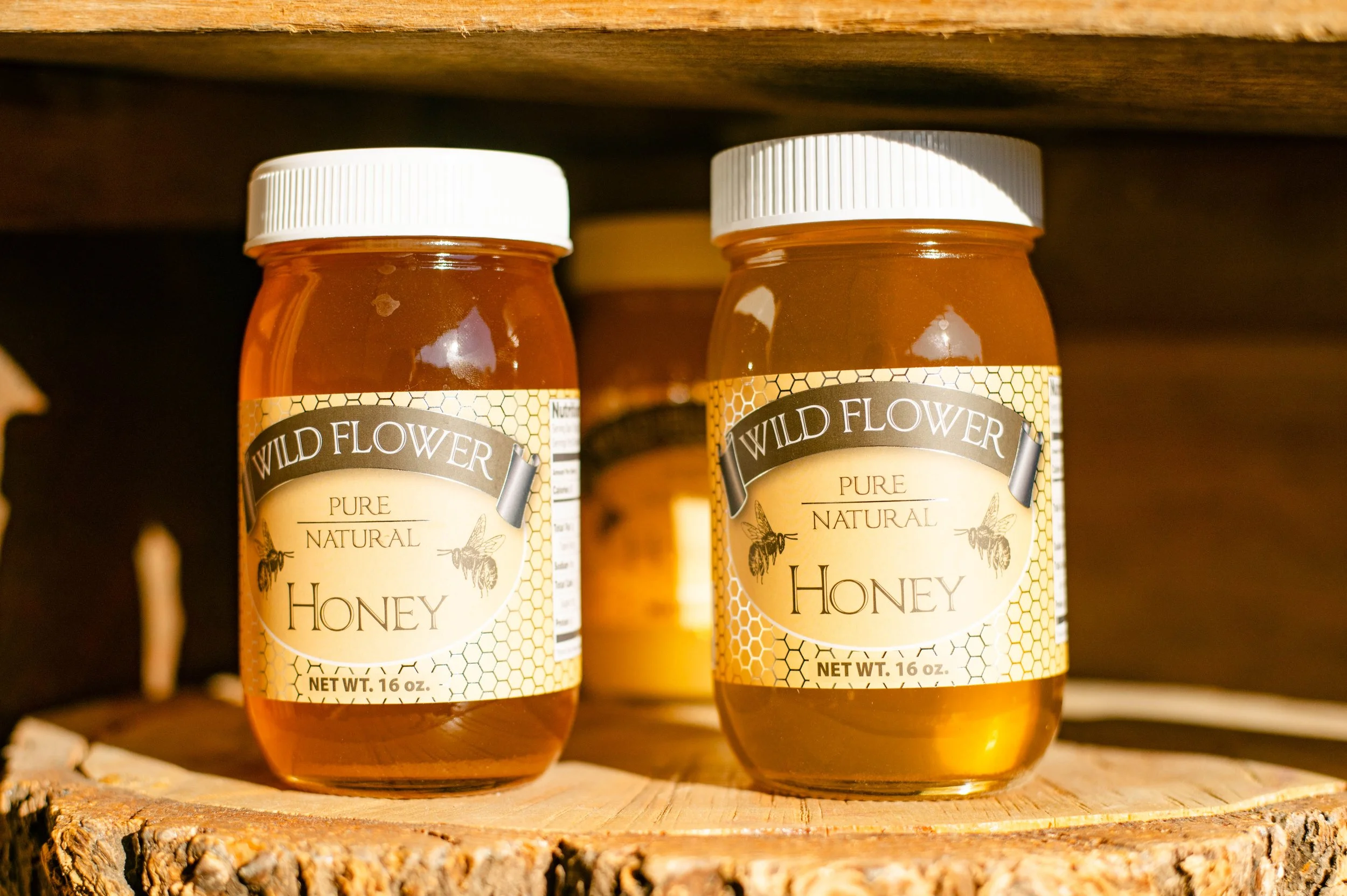Two jars of wildflower pure natural honey on a wooden surface with a darker wooden background.