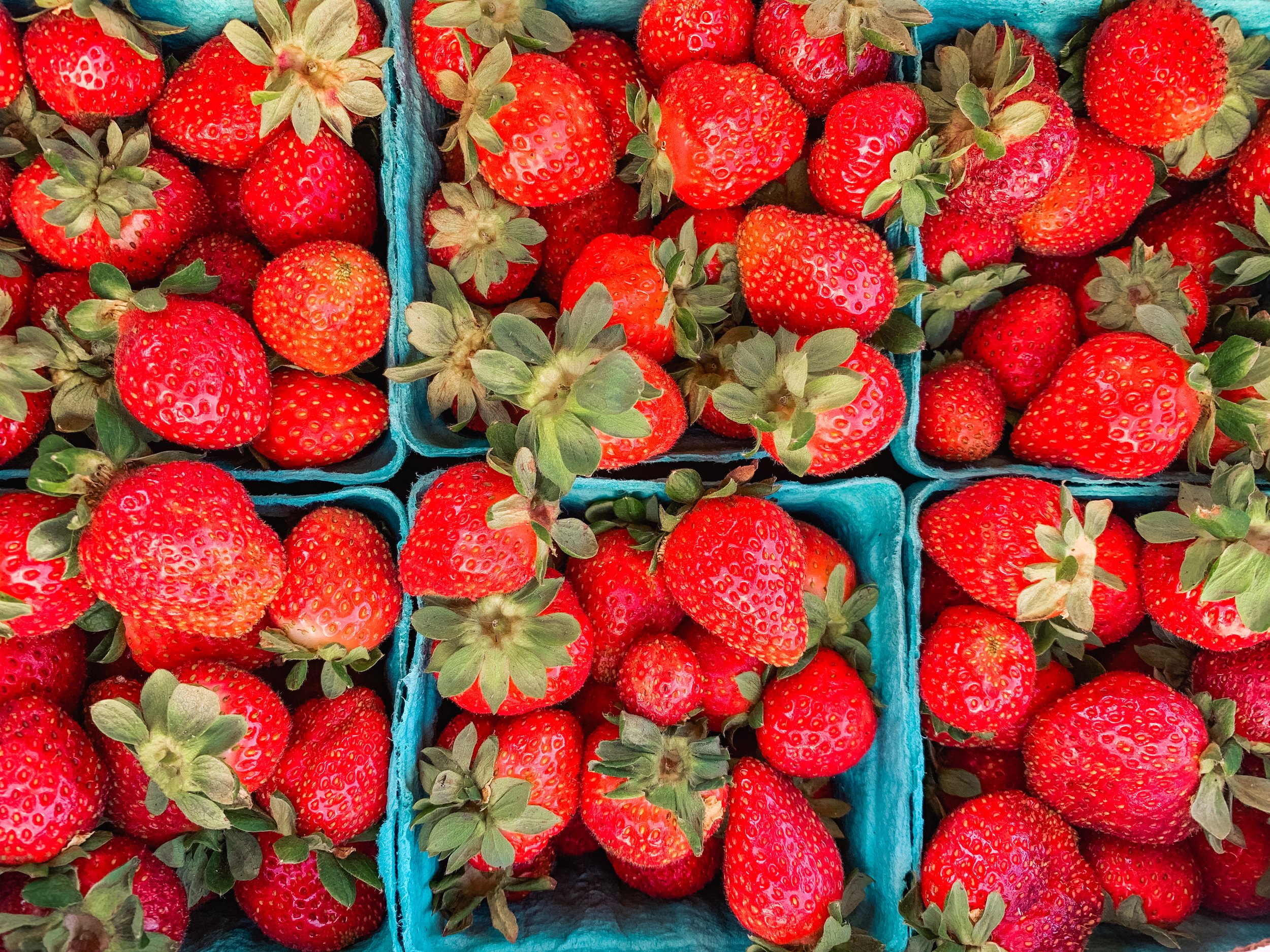 Fresh strawberries with green leaves in blue containers.