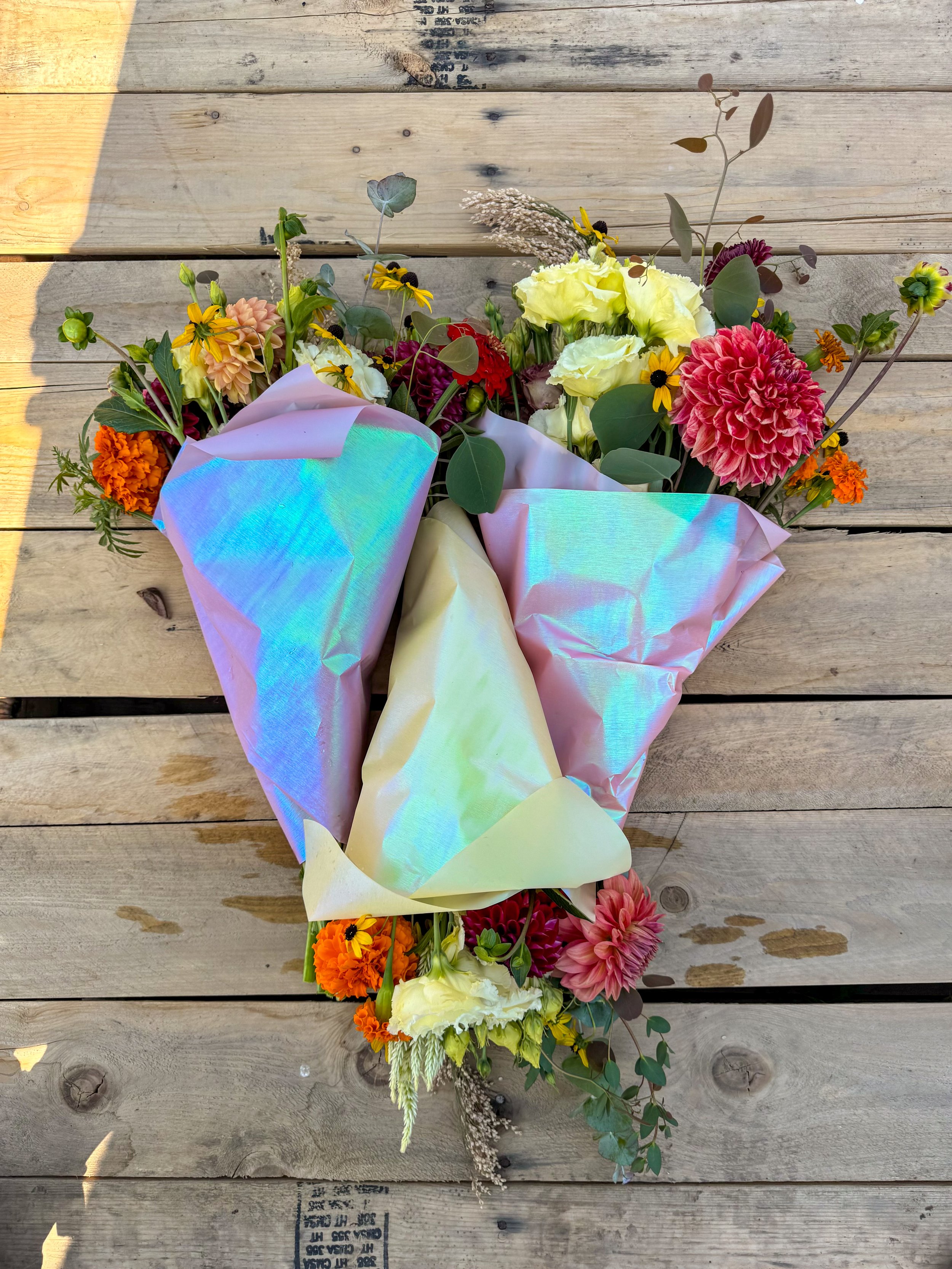 A colorful bouquet of flowers wrapped in iridescent wrapping paper on a wooden surface.
