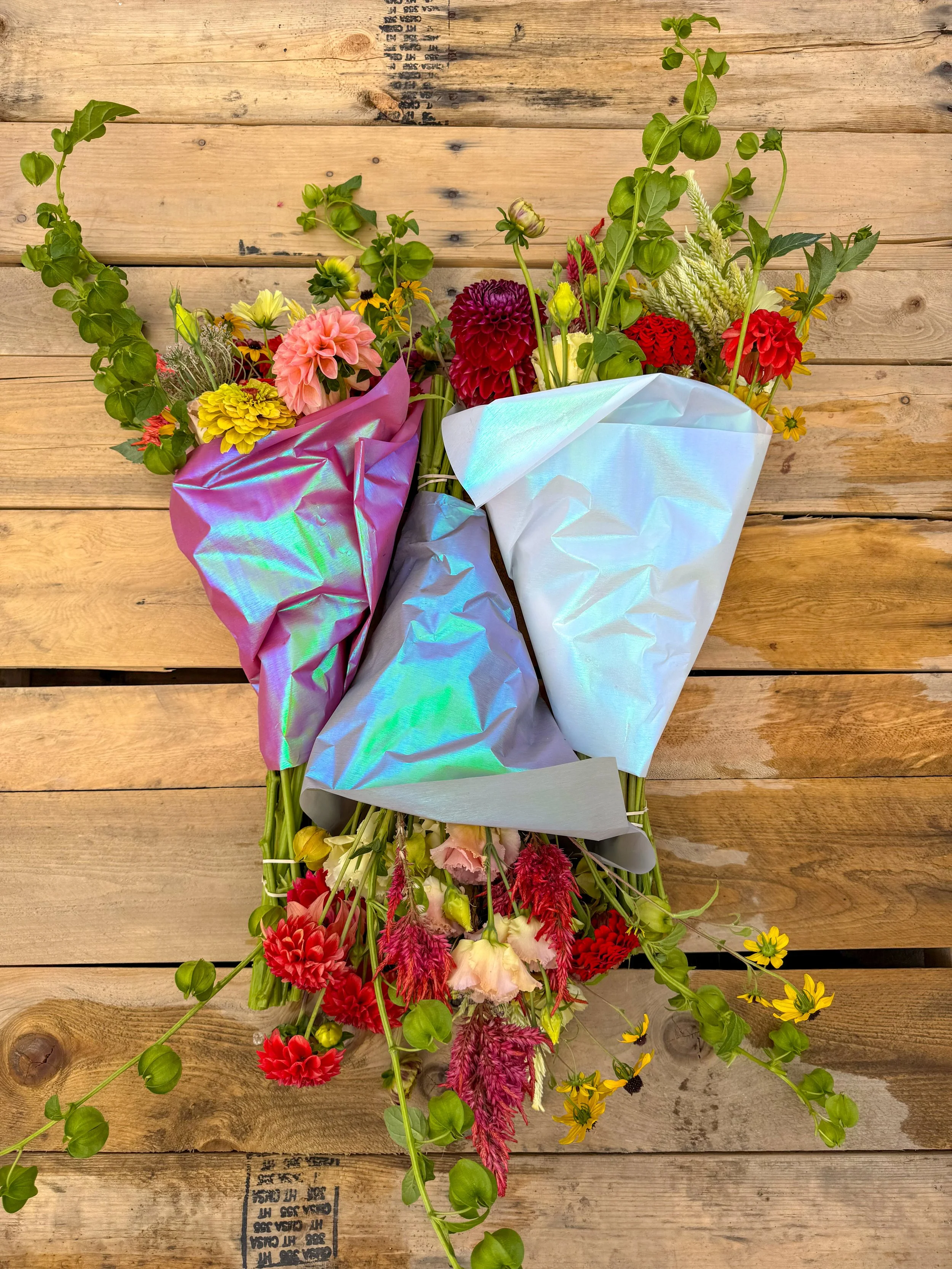 Colorful mixed flower bouquet on a wooden surface wrapped in iridescent paper.