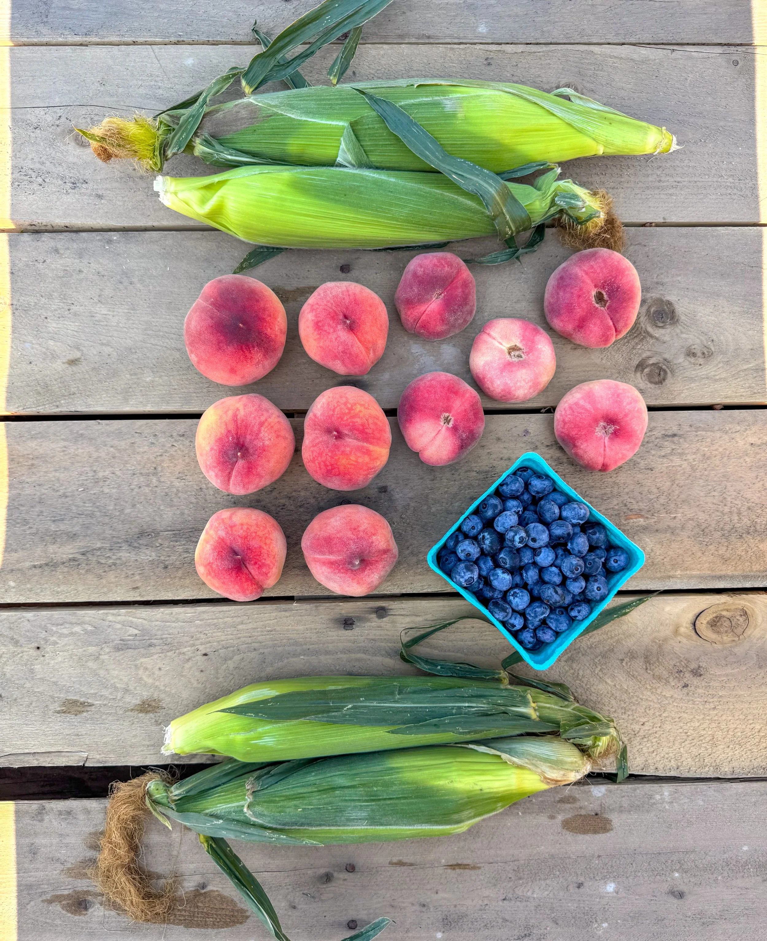 Fresh peaches, blueberries, and ears of corn on a wooden table.