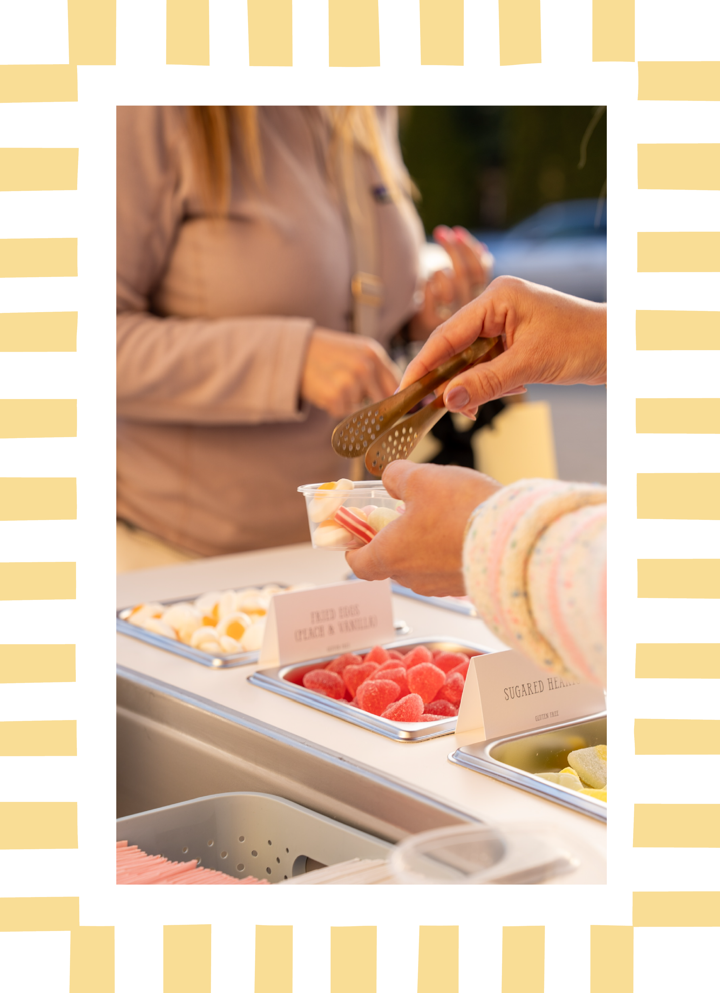 Close-up of a person serving themselves candy from a buffet with various types of candies labeled in front.