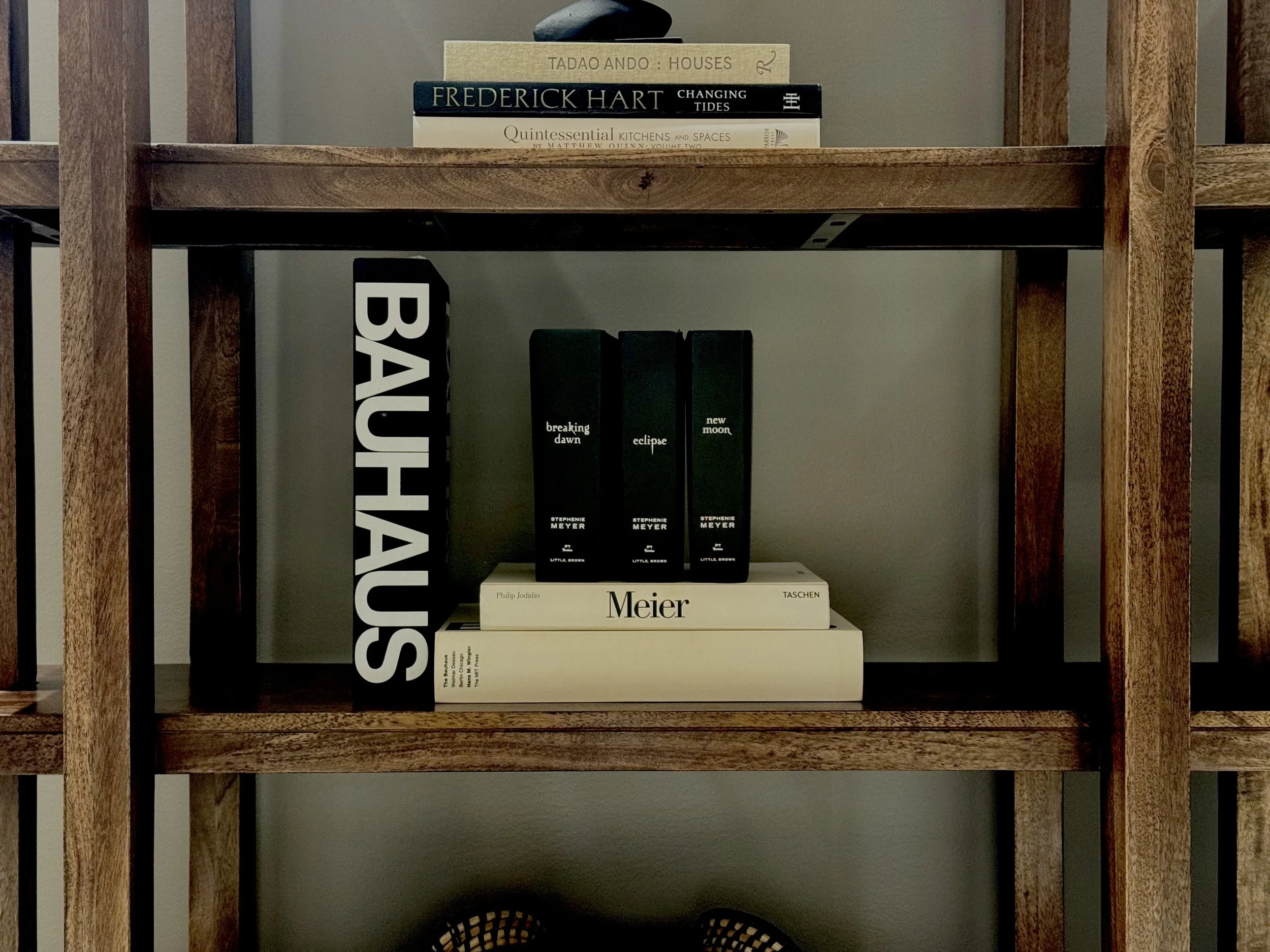 Books on a wooden shelf, including titles on architecture, art, and design, with some standing vertically and others stacked horizontally.