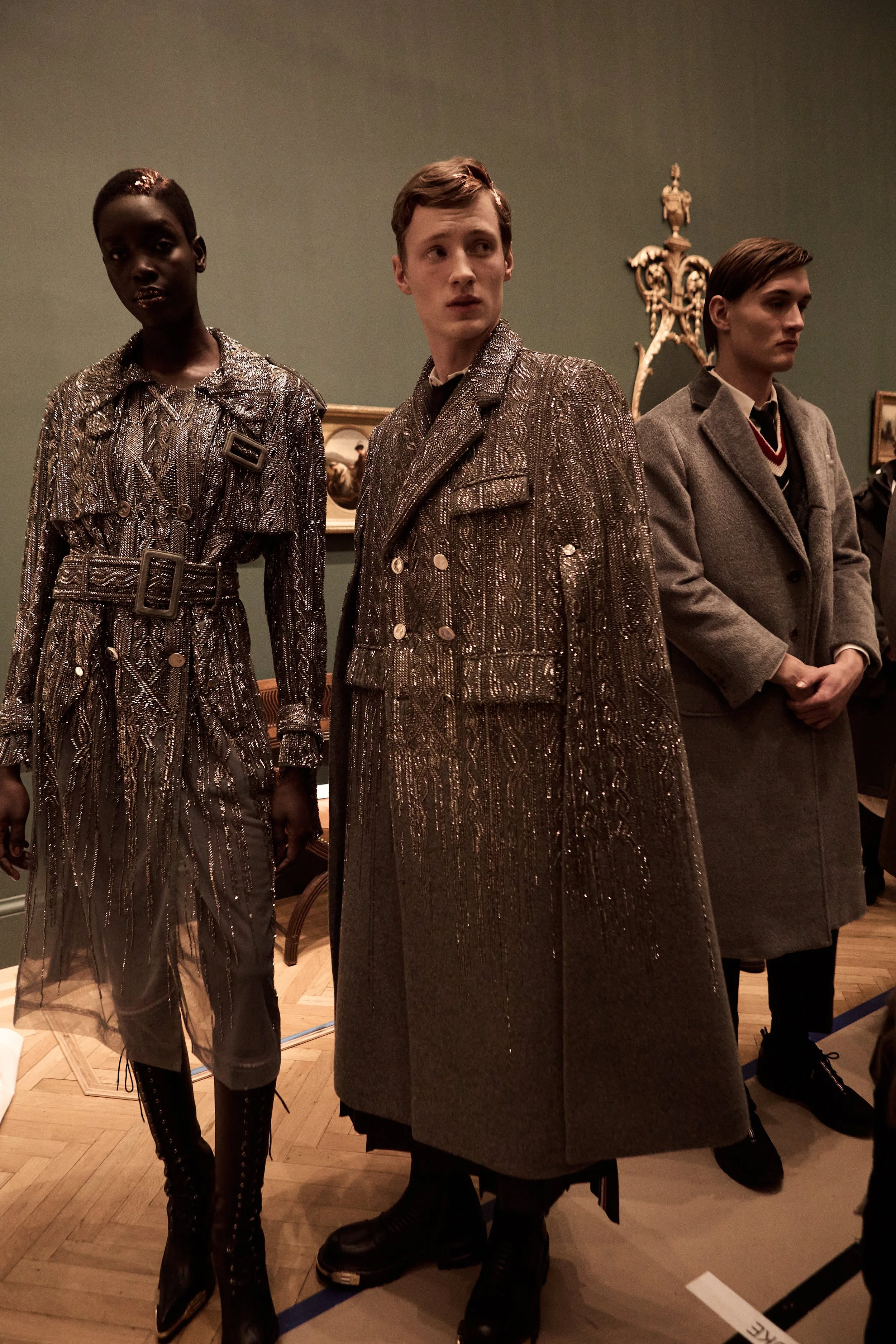 Three models in vintage clothing standing in a room with green walls and wooden floors.