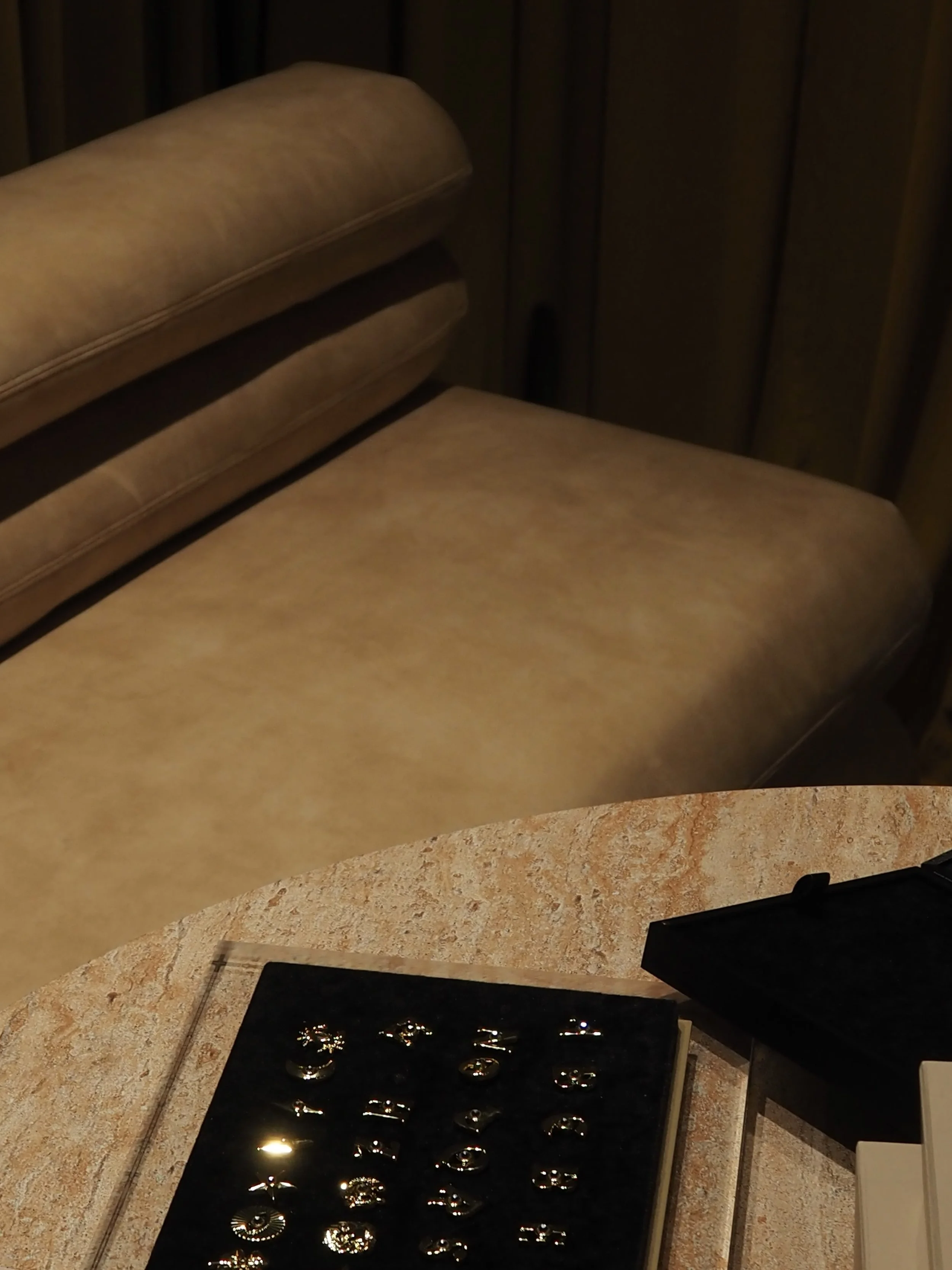 A beige upholstered sofa with wooden paneling in the background at the Hourglass pop-up store opening in Sydney, Australia, and a marble table with jewelry displayed on a black tray in the foreground.