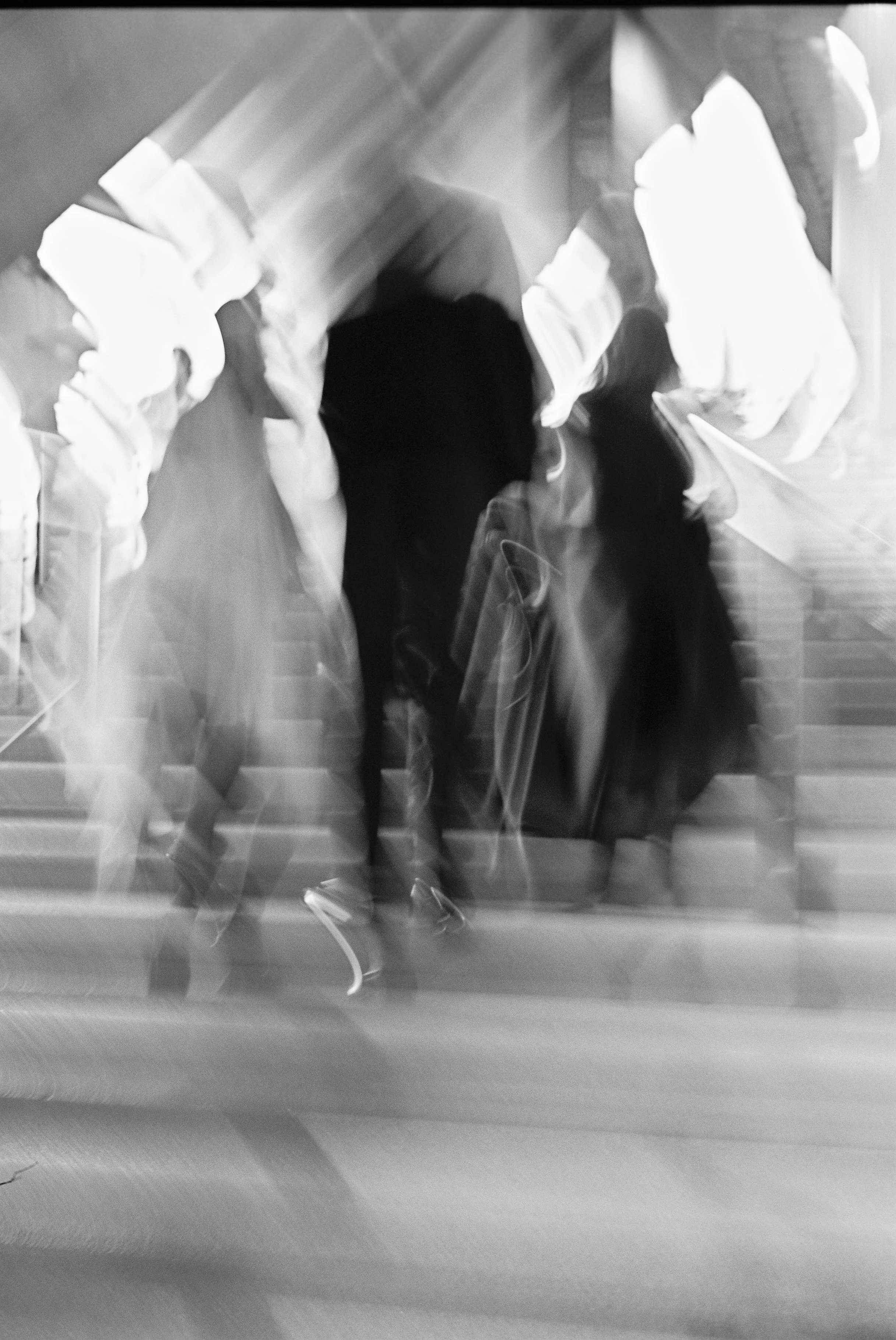 Blurry black-and-white photo of people walking down stairs, with motion blur.