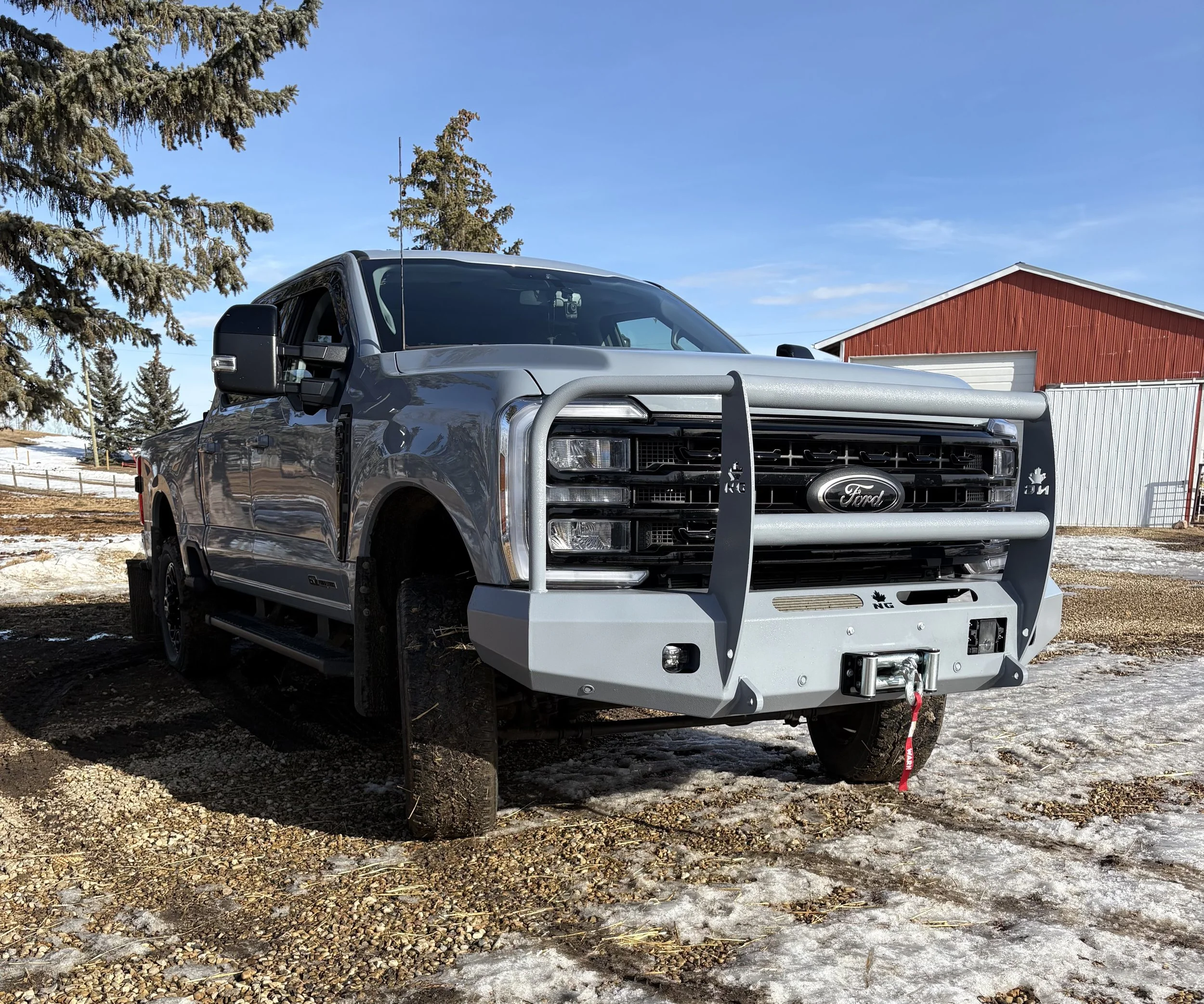 A gray Ford pickup truck with a large silver-colored front bumper and grille guard, parked outdoors on a partially snow-covered ground.