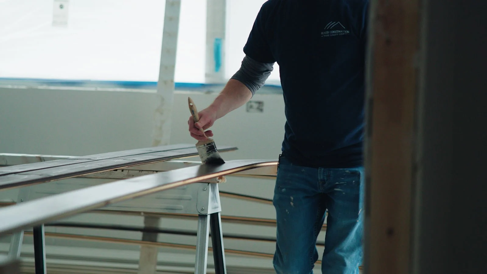 Person painting a curved wooden piece in an indoor construction setting.