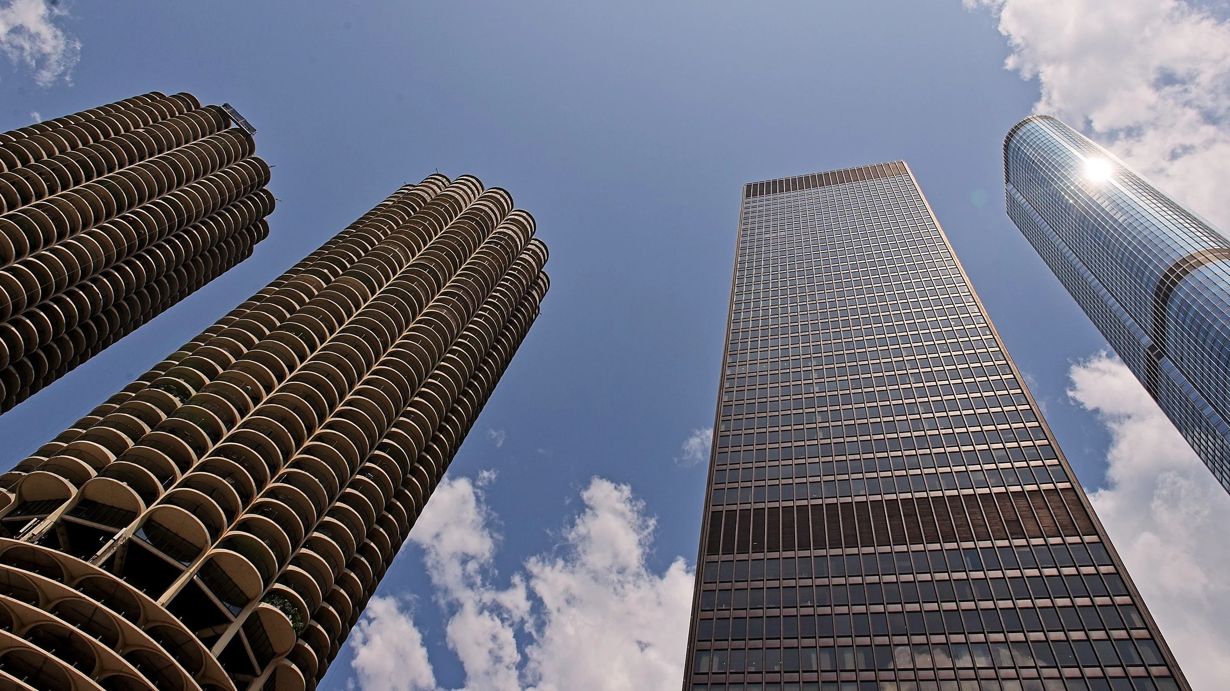 Looking up at four tall skyscrapers against a partly cloudy sky.