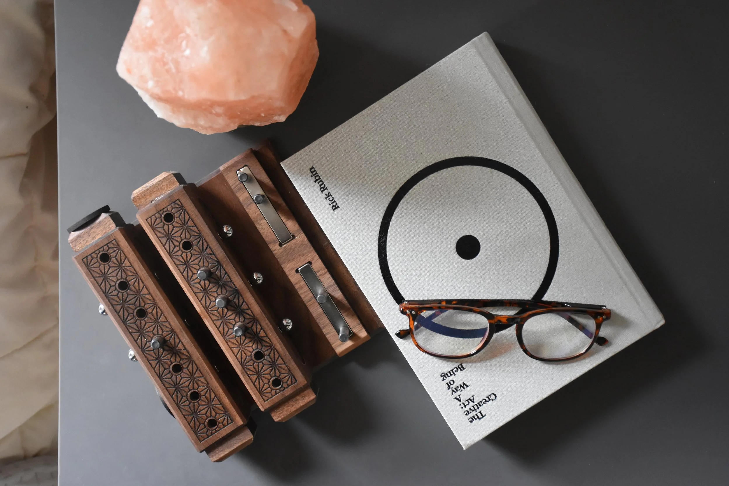 A Ruthenium vinyl record book, a pair of tortoiseshell eyeglasses, a salt lamp, and a wooden zylophone with patterned carvings on a black surface.