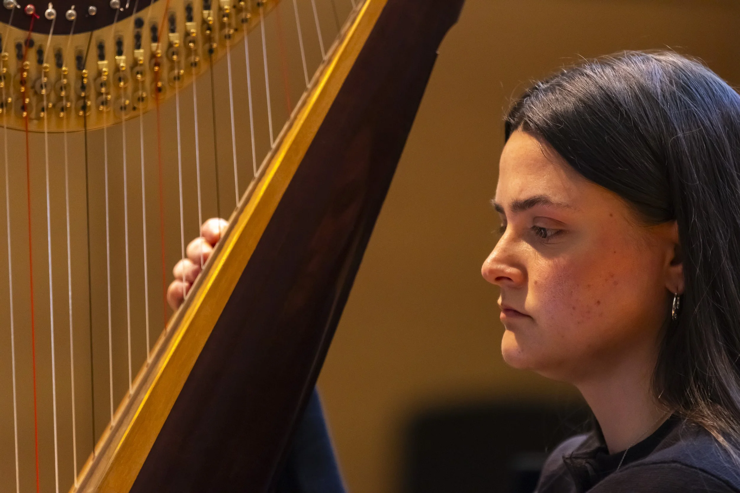 Close-up of a young woman playing a harp, focusing on her face and the strings.