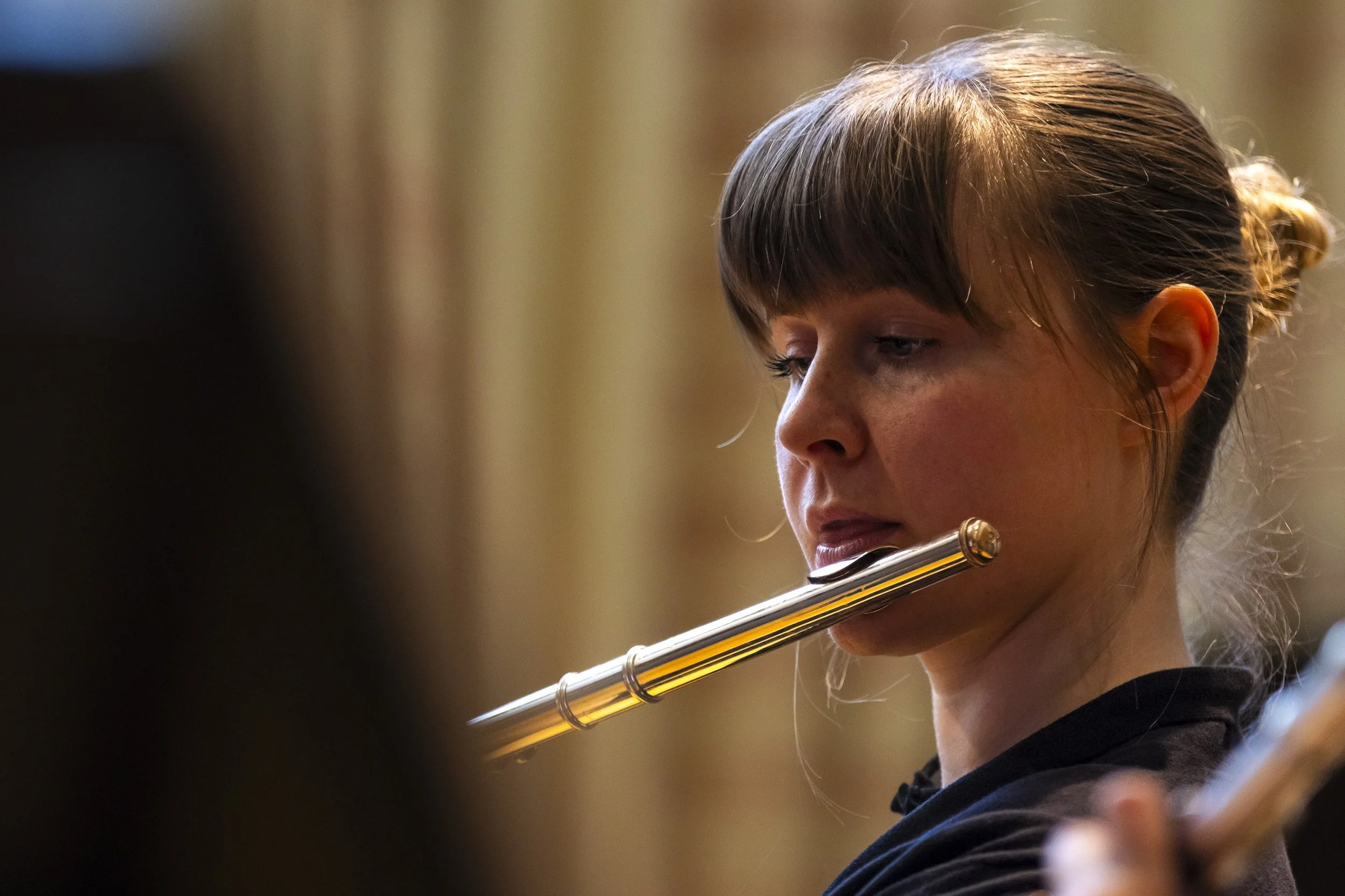 A young woman with brown hair tied back, playing a silver flute.