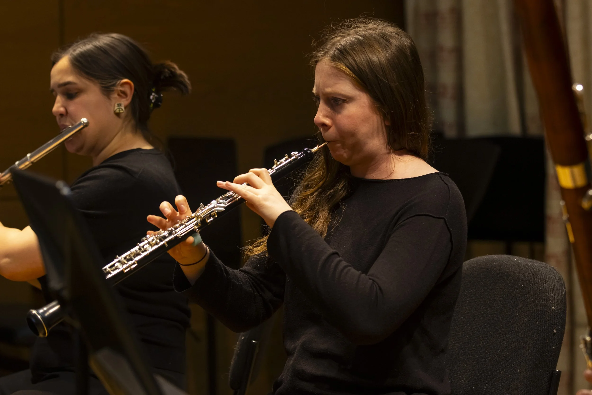 Two women playing flutes during a performance in an indoor setting.