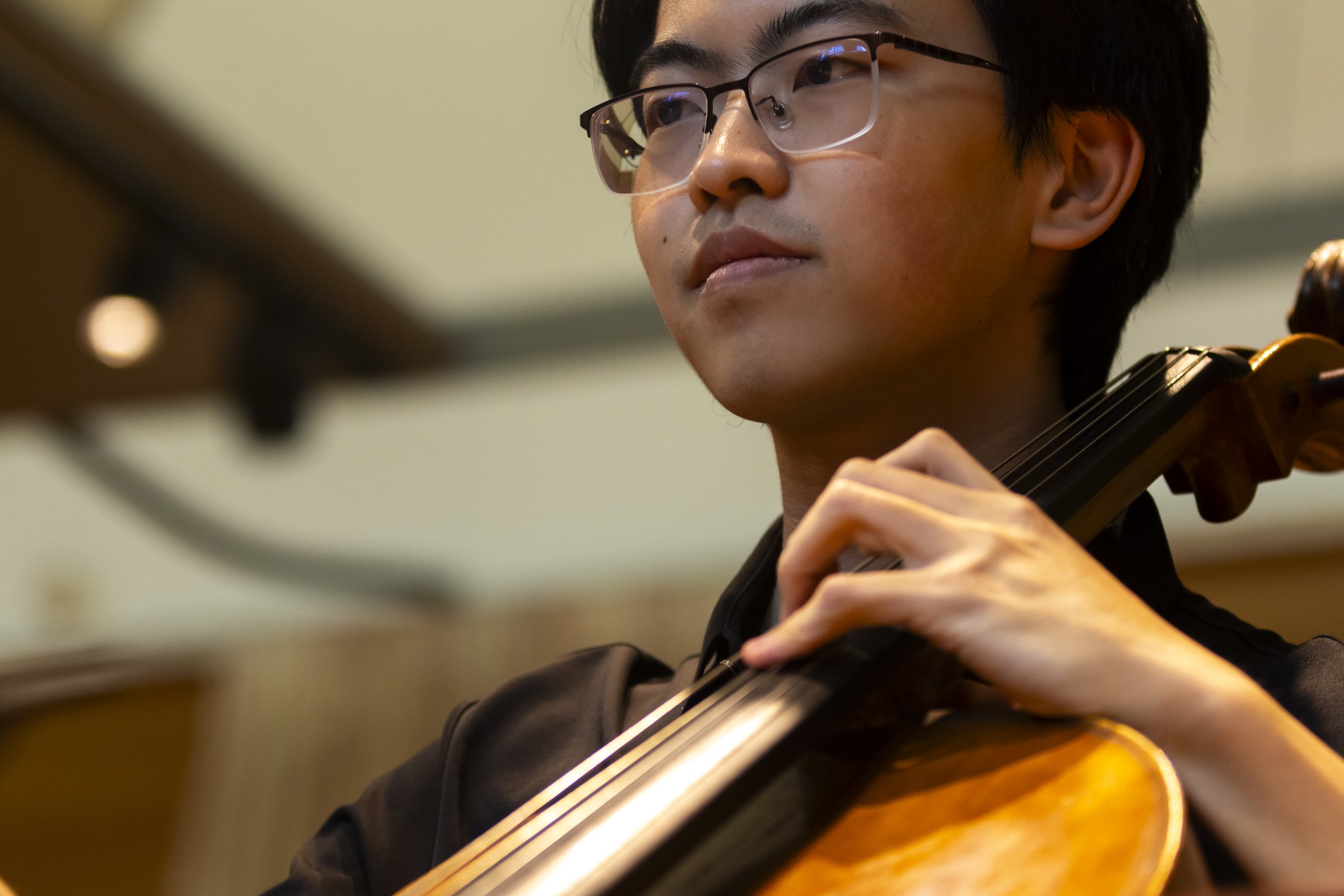 A young man with glasses playing the violin indoors.