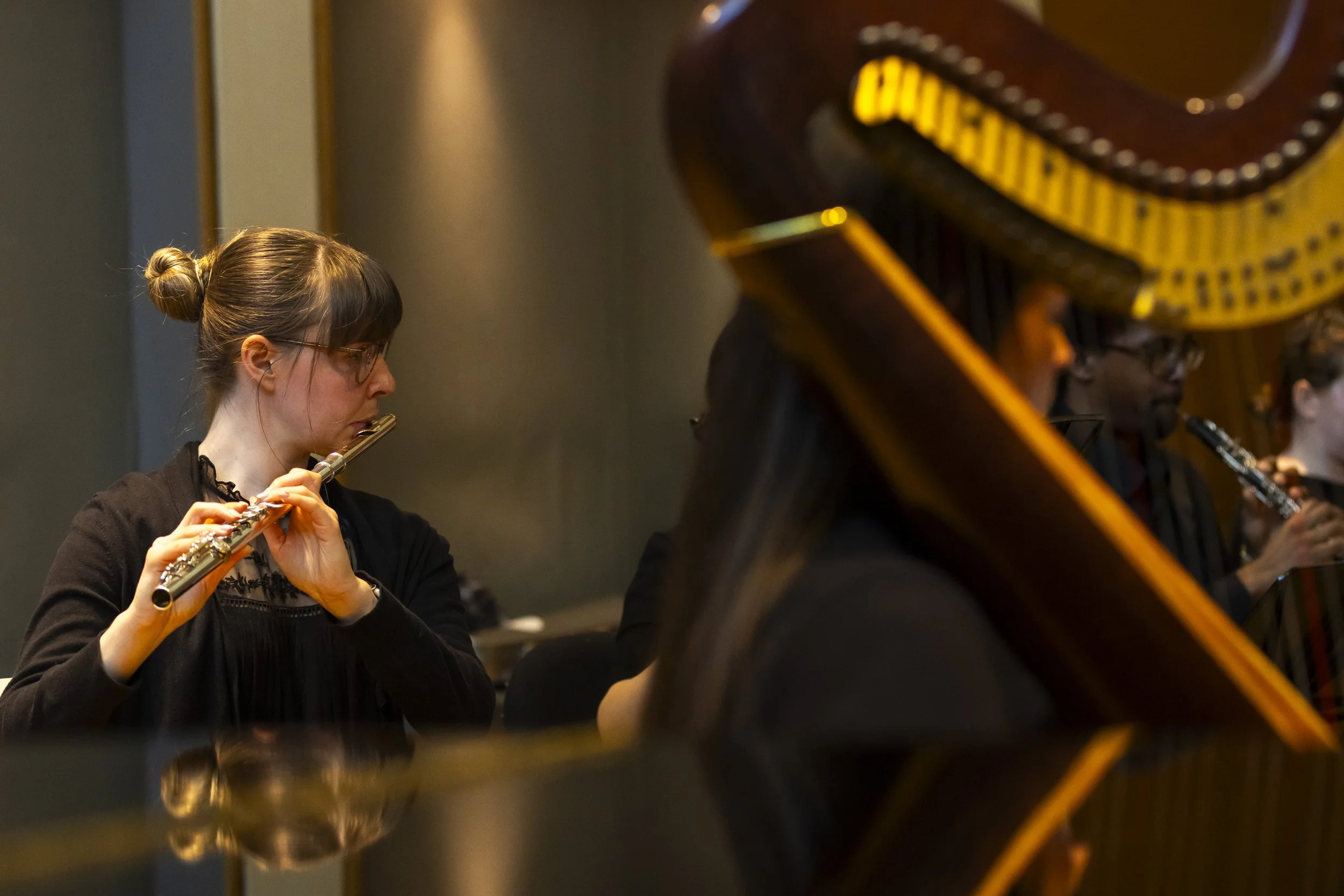 A woman playing the flute in a group performance, with other musicians visible in the background.