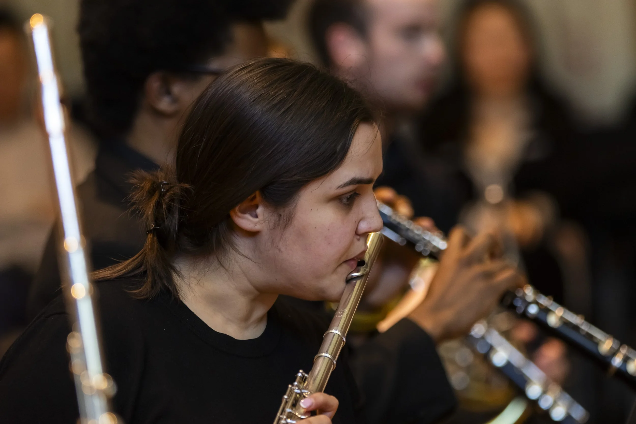 Young woman playing a flute in an orchestra with other musicians in the background.