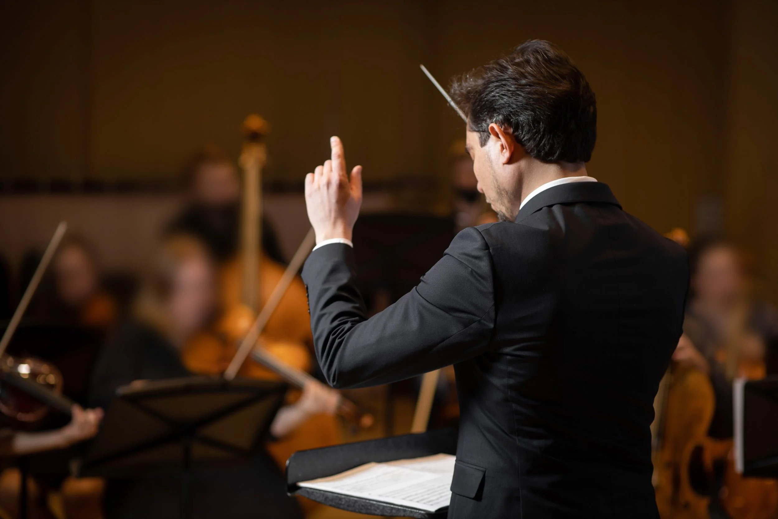 Conductor leading an orchestra in a concert hall.