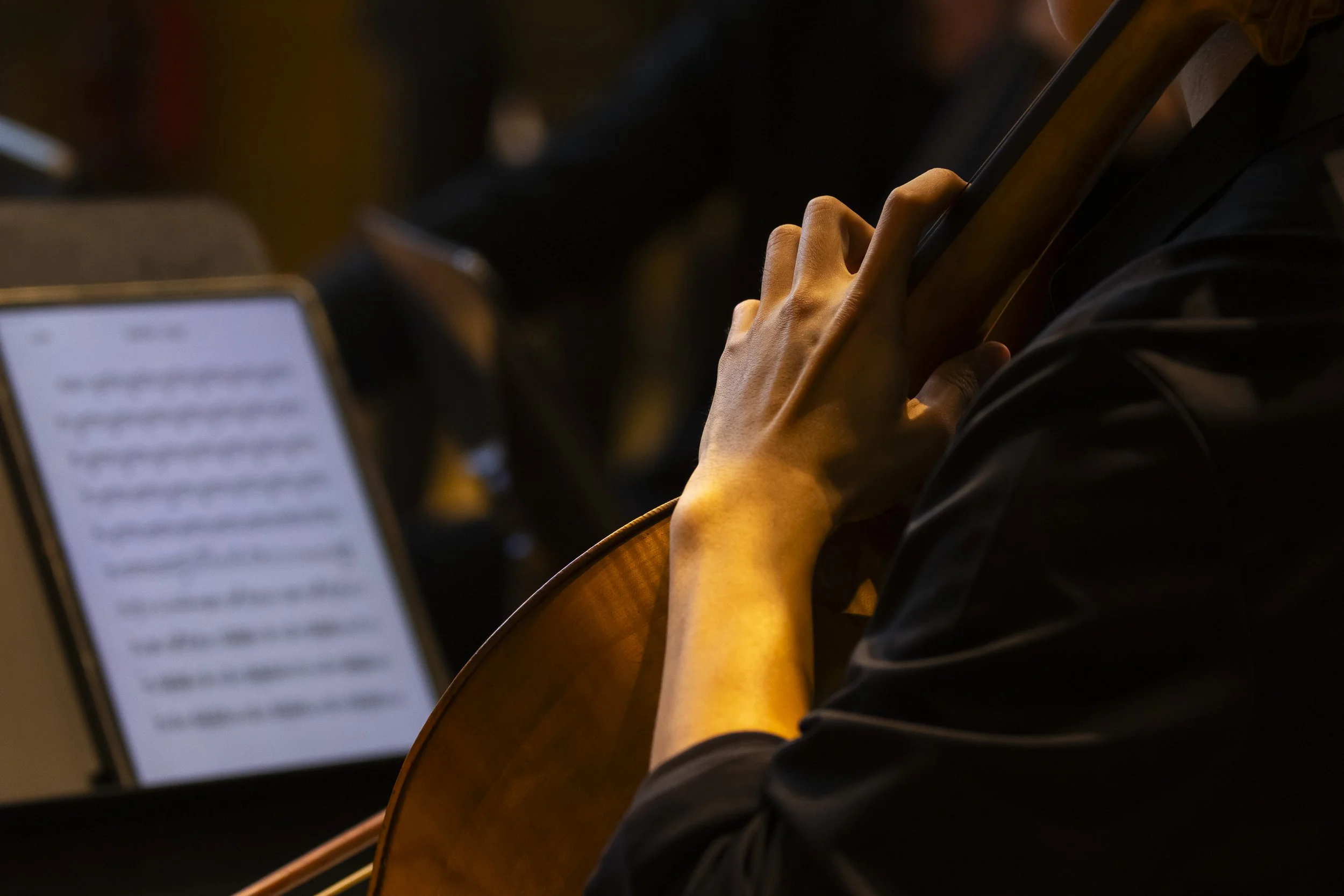 Close-up of a person's hand holding a smartphone while sitting at a table with a music stand in the background.