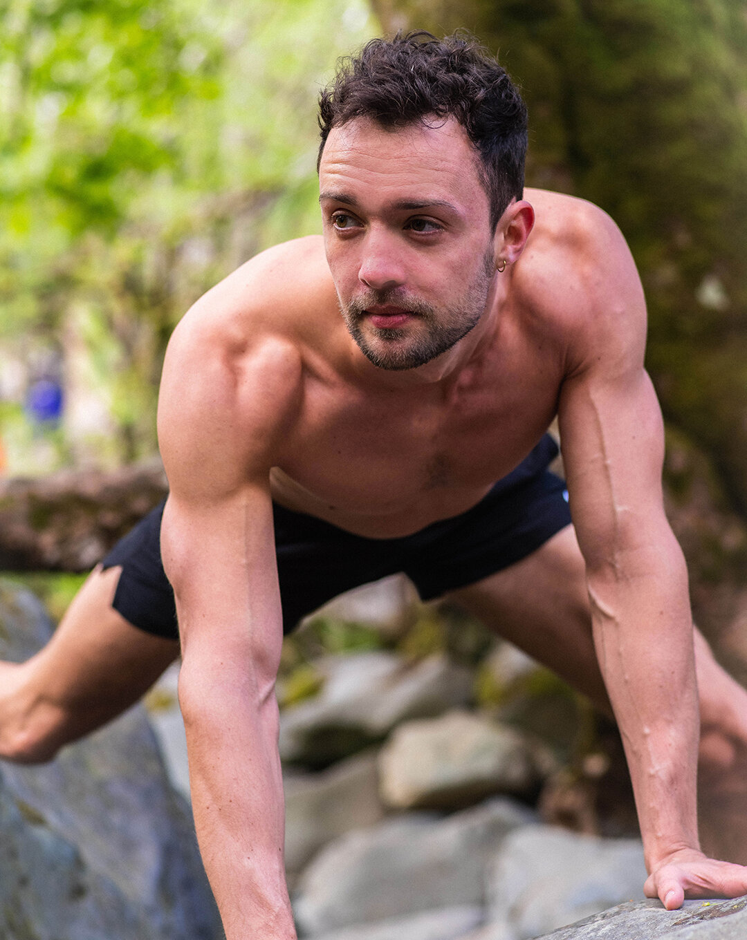 Personal Trainer outdoors exercising on rocks, shirtless, wearing shorts, in a push-up position.
