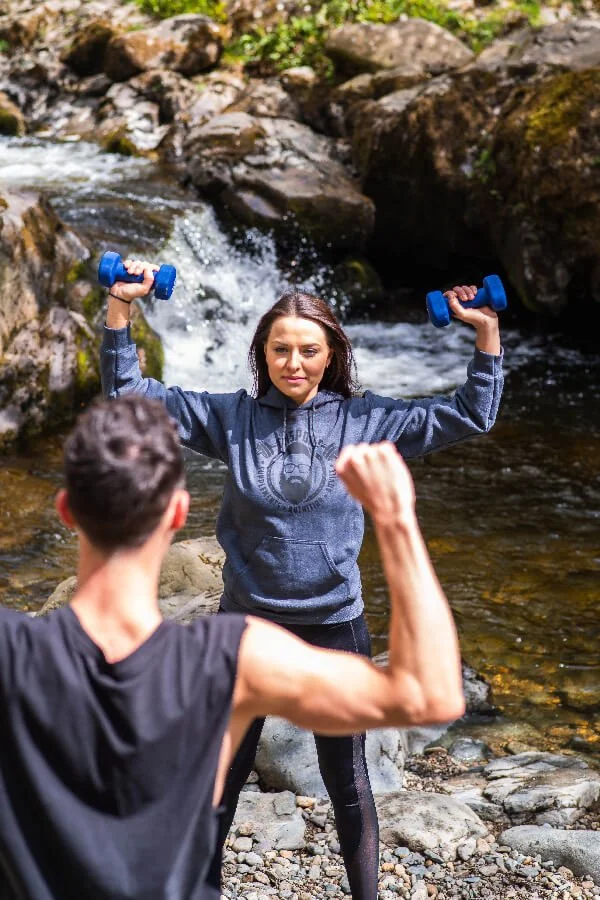 Personal Trainer training client with dumbbells near a river