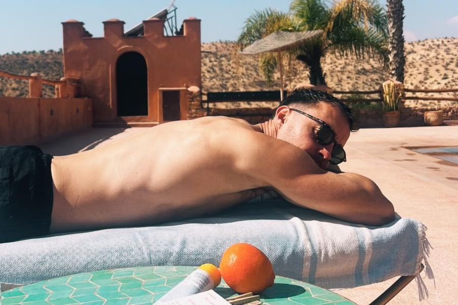 Personal Trainer Lying on Sunbed in Morocco with an Orange Fruit