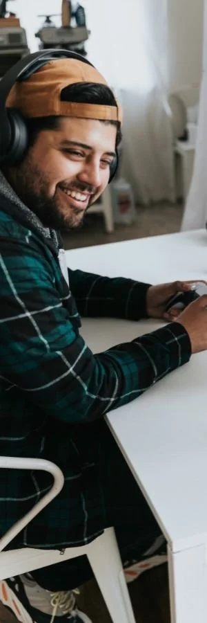 Mindset Coaching client wearing headphones and a cap, smiling while sitting at a desk and holding a gaming controller.