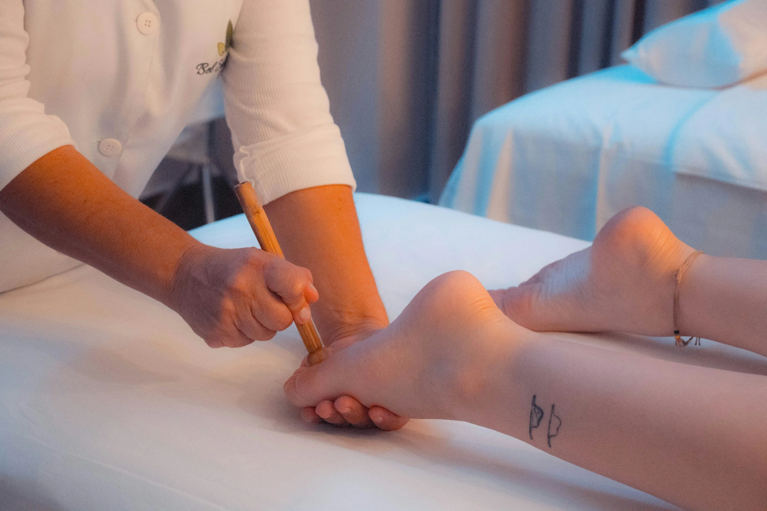 A person wearing a white medical coat and latex gloves performing a procedure on a patient lying on a medical bed, with a pen or instrument in hand and medical equipment visible in the background.