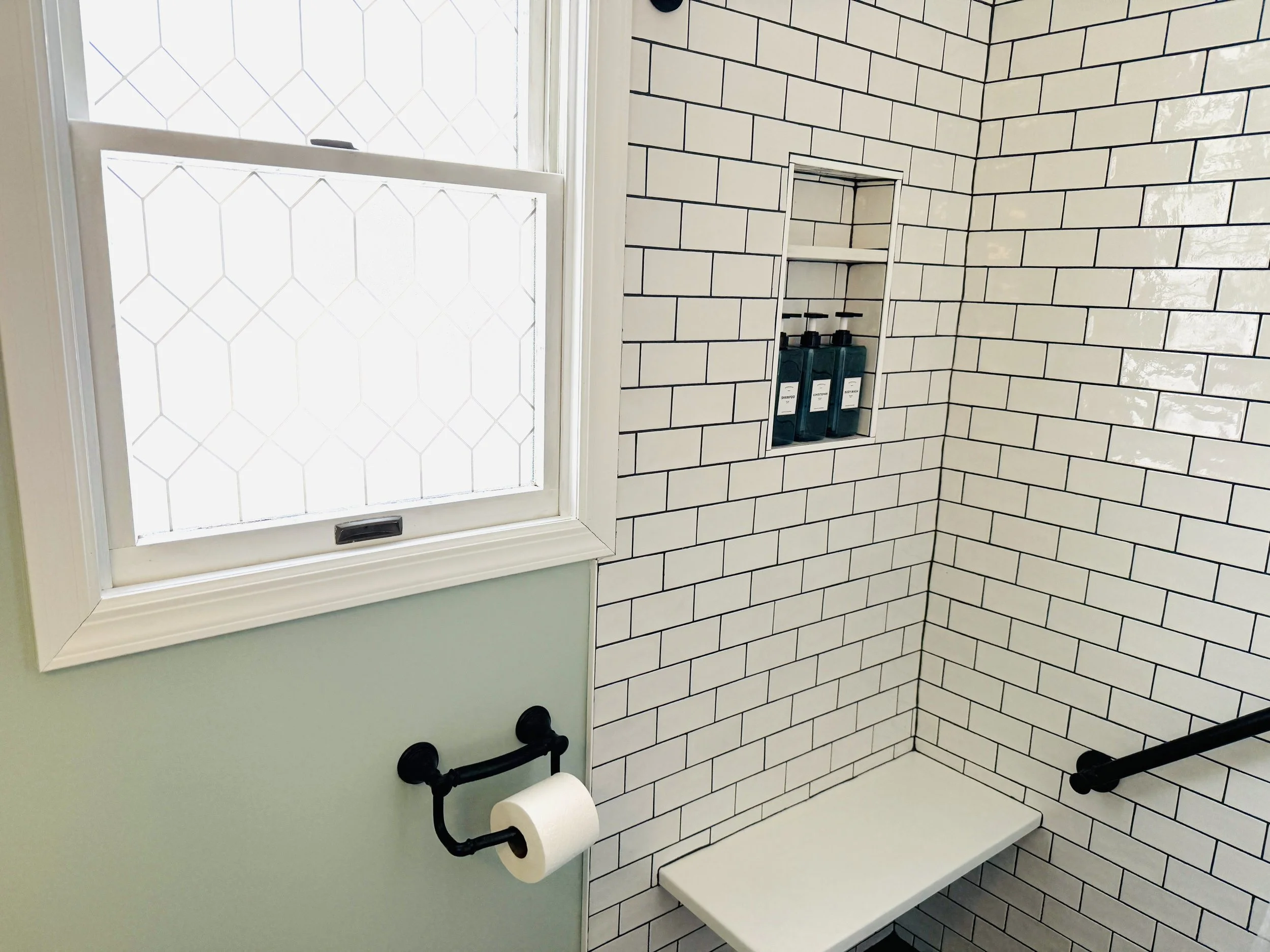 A shower area with white subway tiles and a small built-in shelf holding three bottles of rinse.
