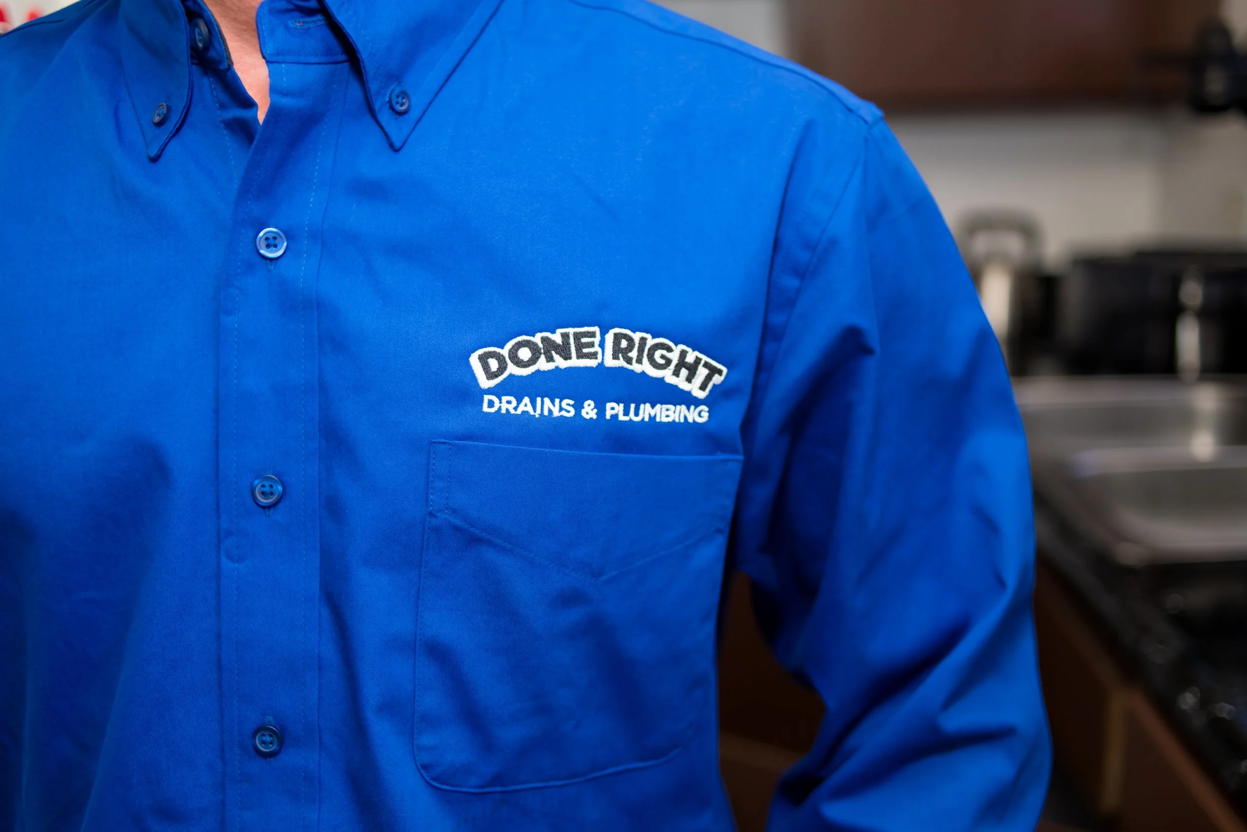 Close-up of a person wearing a blue button-up shirt with a logo that reads 'DONE RIGHT DRAINS & PLUMBING'.