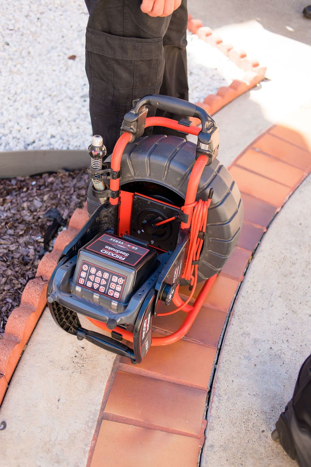 A paving machine placed on a curved brick border, with a person's body partially visible behind it.