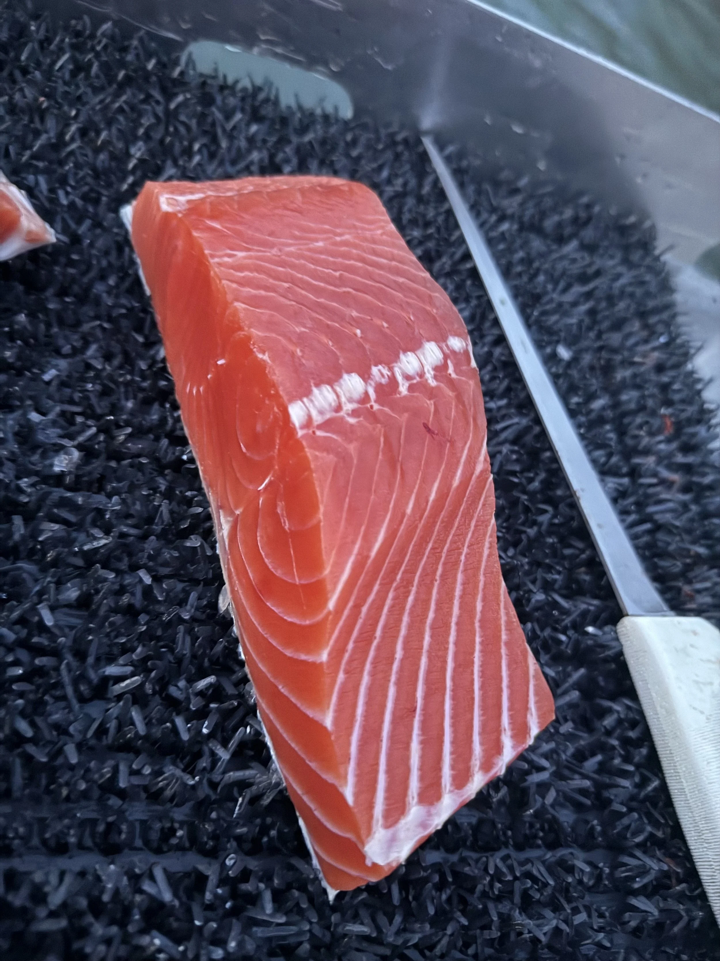 Fresh, raw salmon fillet on a bed of black rice with a carving knife beside it.