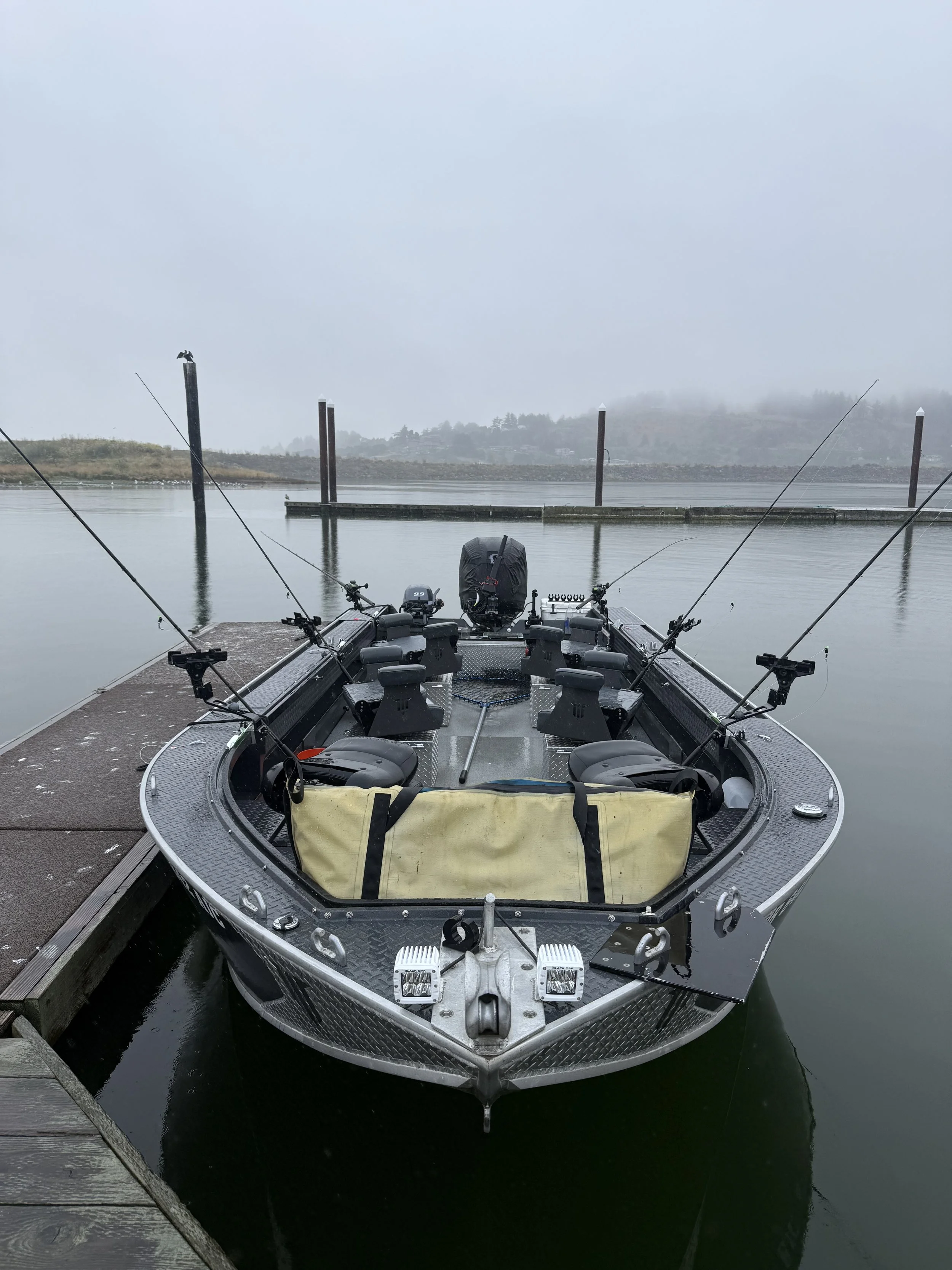 A fishing boat docked at a pier on a foggy day, with four fishing rods mounted on the boat.