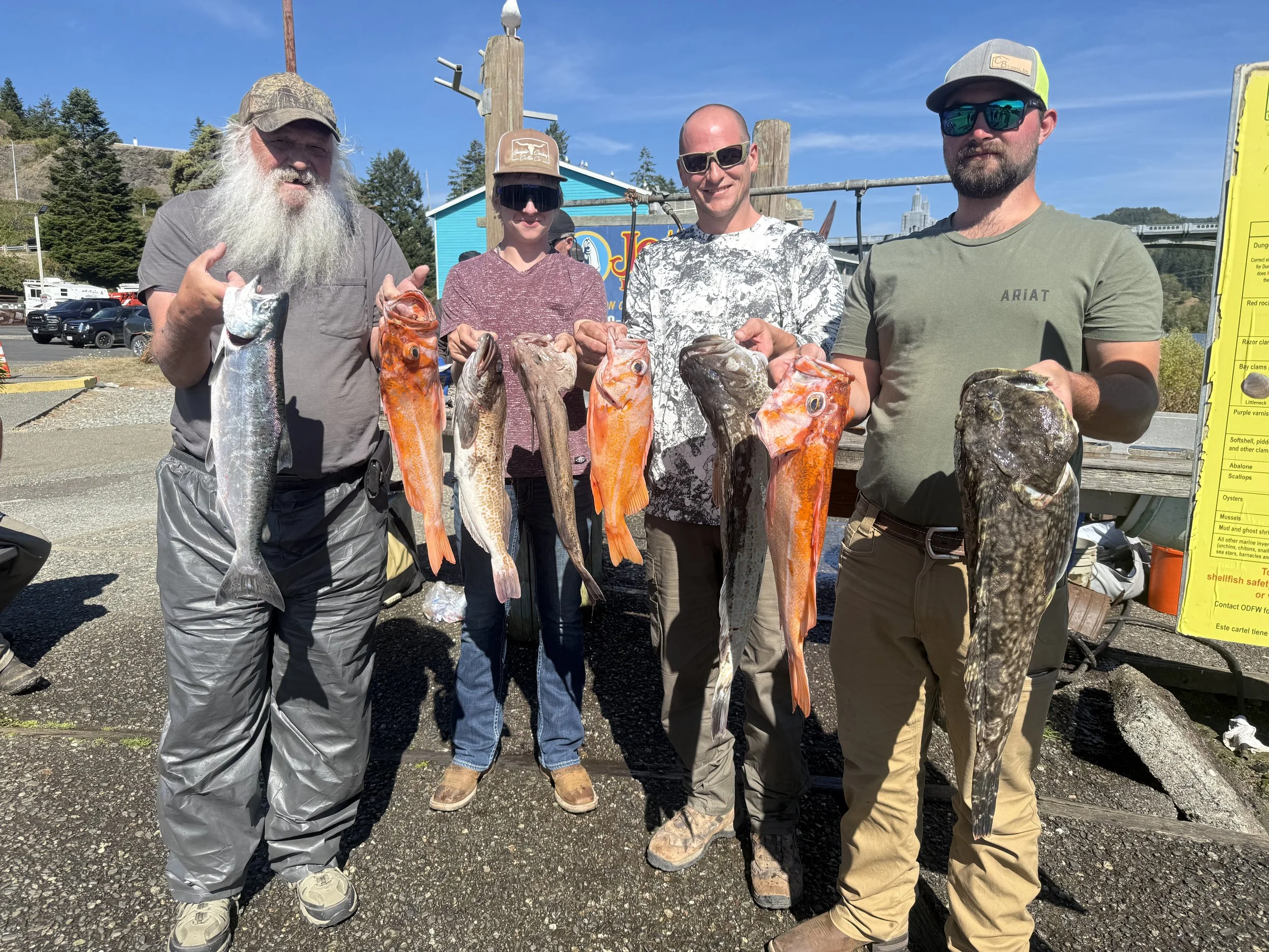 Five people displaying their fresh catch of various fish, standing outdoors on a sunny day.